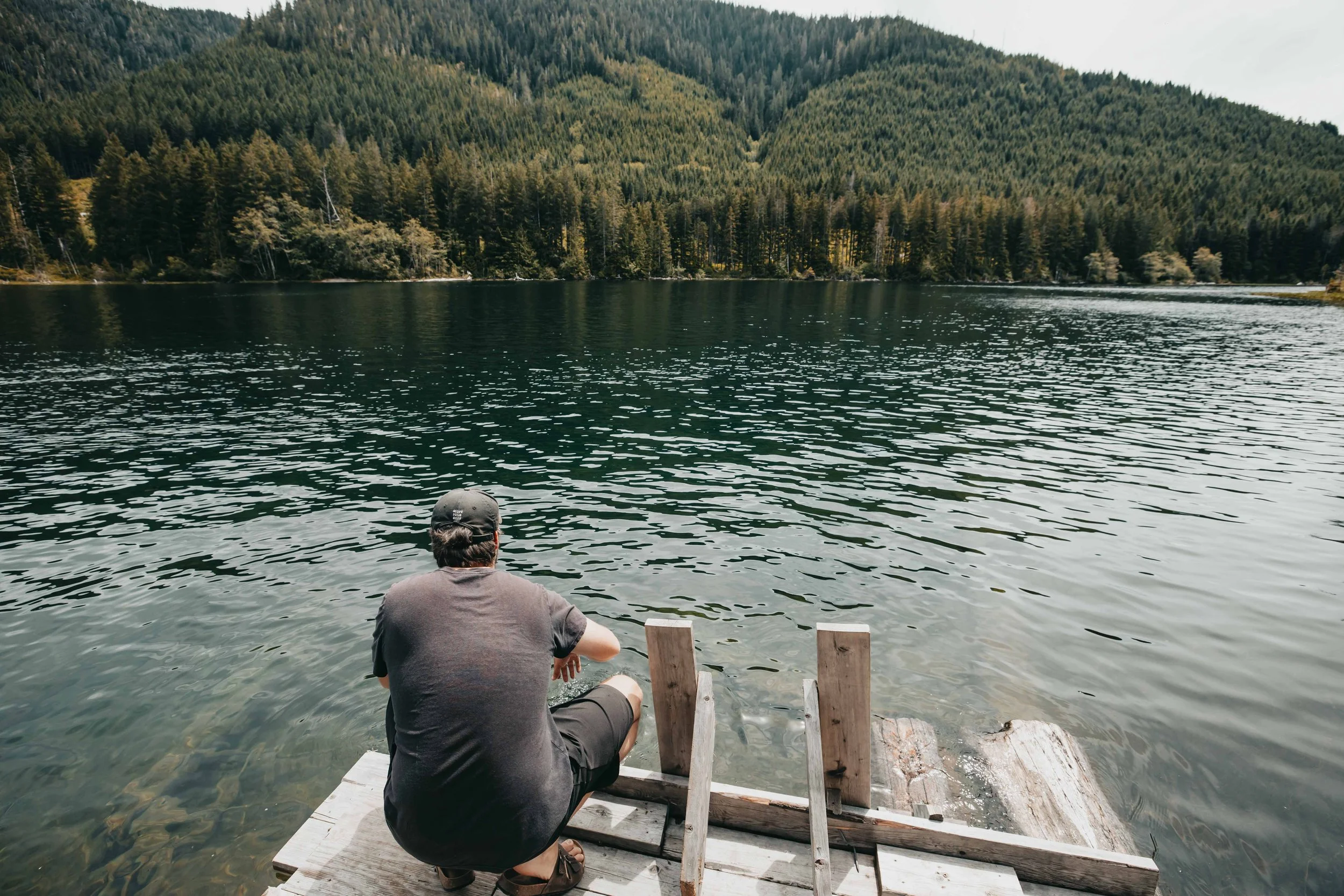 a man kneels on a dock testing the water of a green lake on vancouver island british columbia
