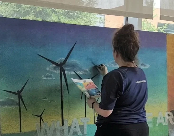 Person painting a mural with wind turbines and a gradient sky