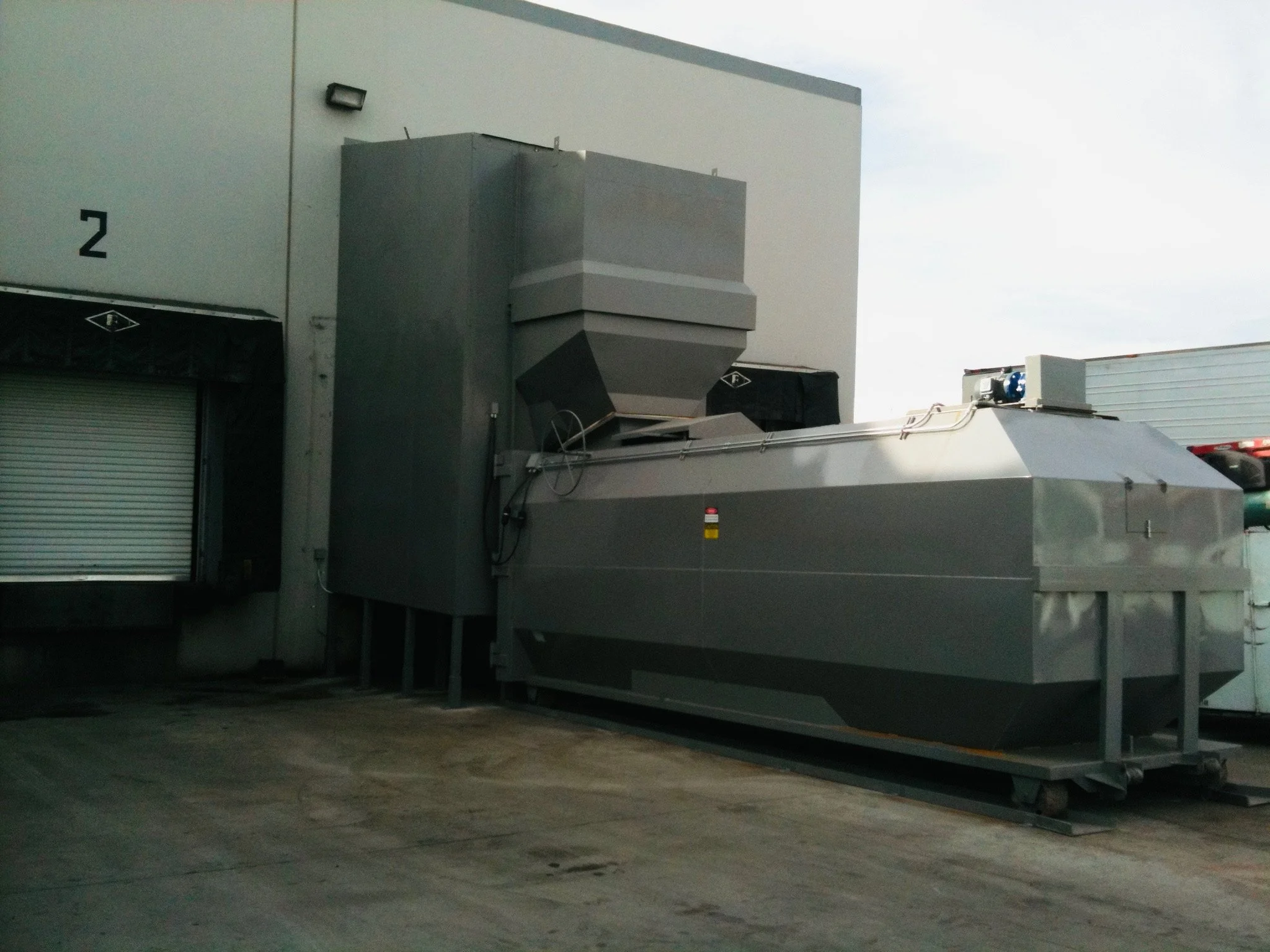 Industrial air handling or HVAC equipment installed outside a building, with a gray metal ventilation hood and duct system, under a cloudy sky.