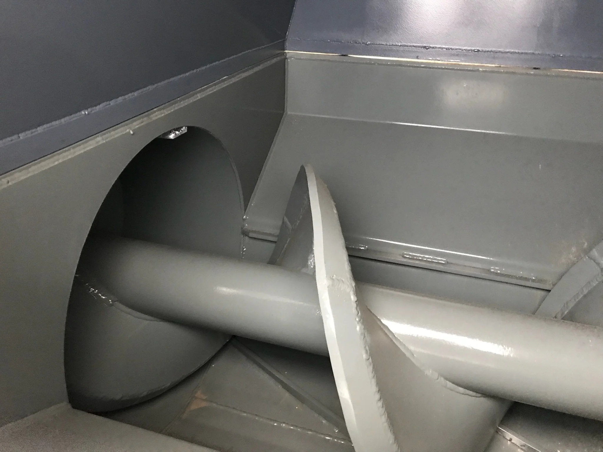 Close-up of gray metallic industrial machine parts with overlapping panels and a rounded vent or opening.