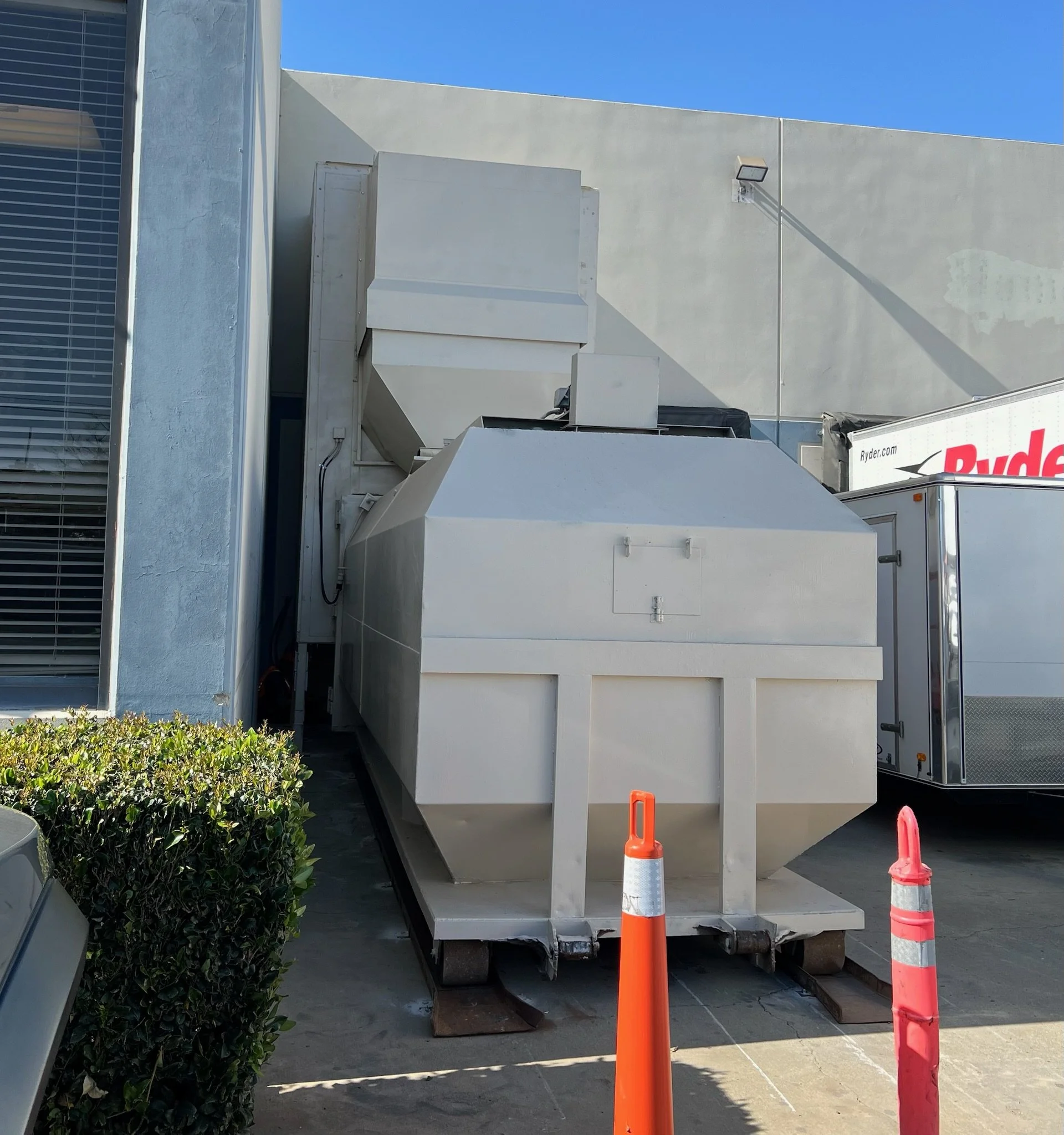 White commercial delivery truck with orange traffic cones in front, parked outside a building with blue sky.