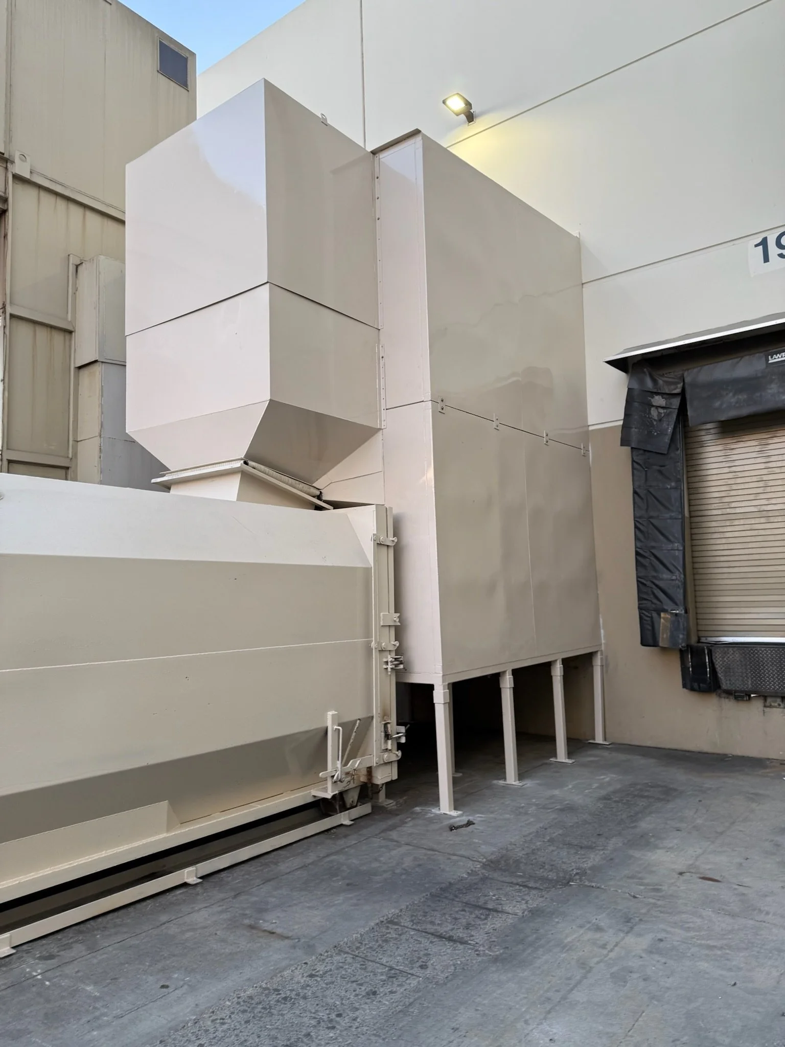 Large industrial metal structure with a white exterior, situated outside a building near a roll-up door with black protective covering.