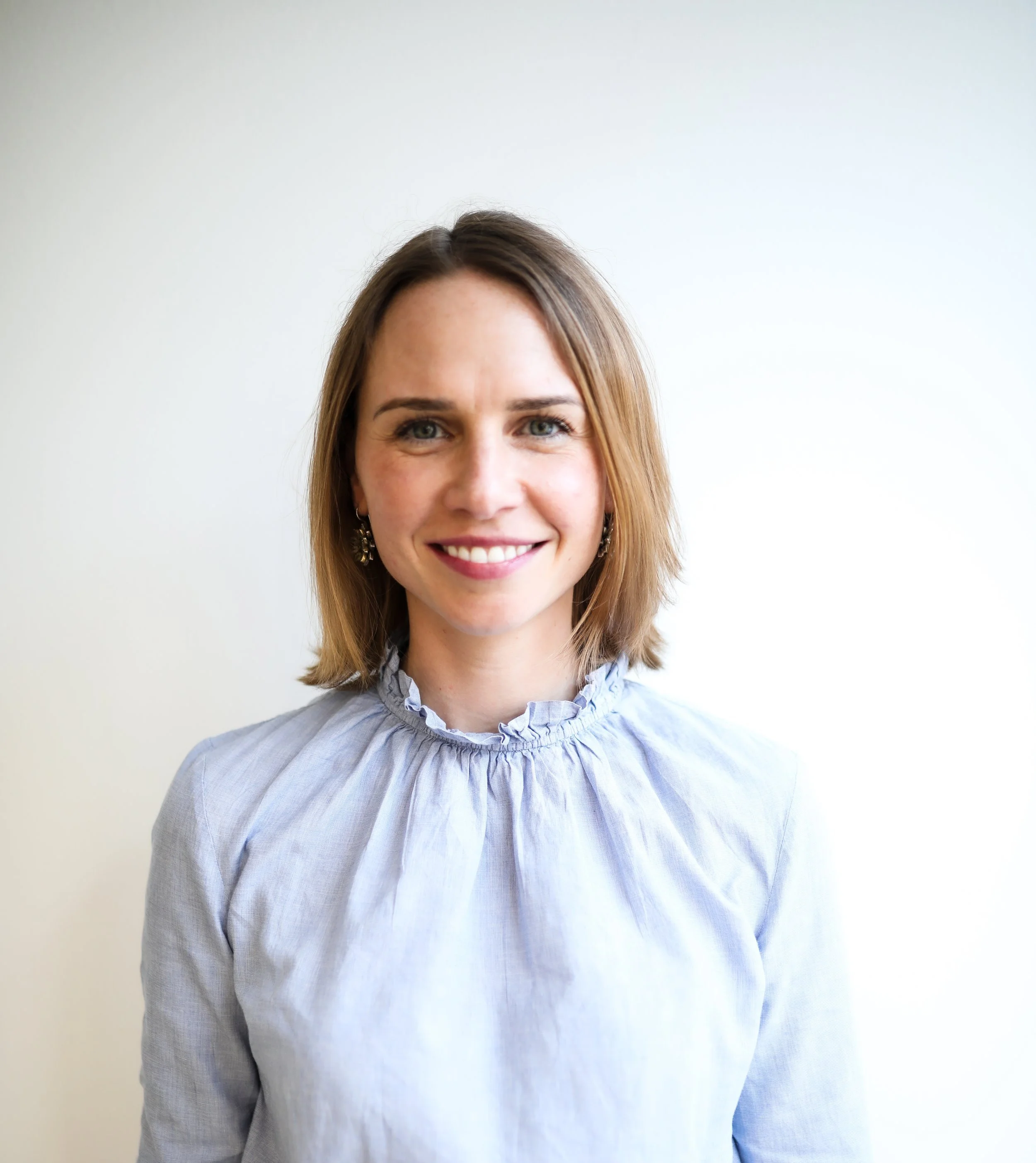 Person with short hair wearing plaid shirt standing outside with cityscape in the background.