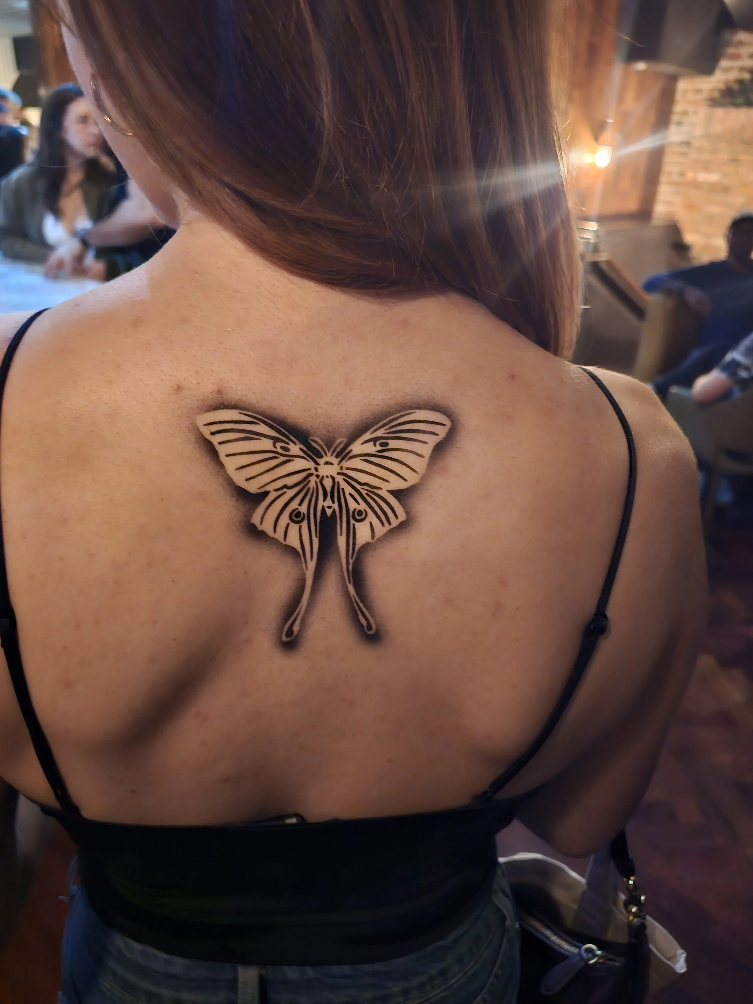 Airbrush tattoo artist creating bold temporary body art for adults at a nightclub or festival event.