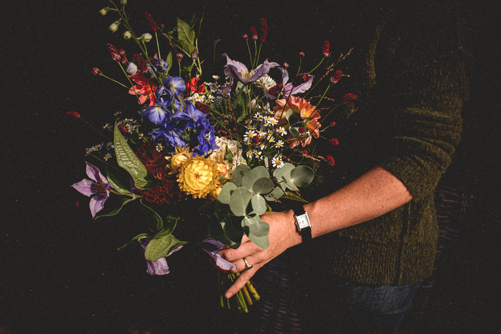 Persoon houdt een kleurrijk boeket bloemen vast, met diverse soorten en kleuren, tegen een donkere achtergrond.