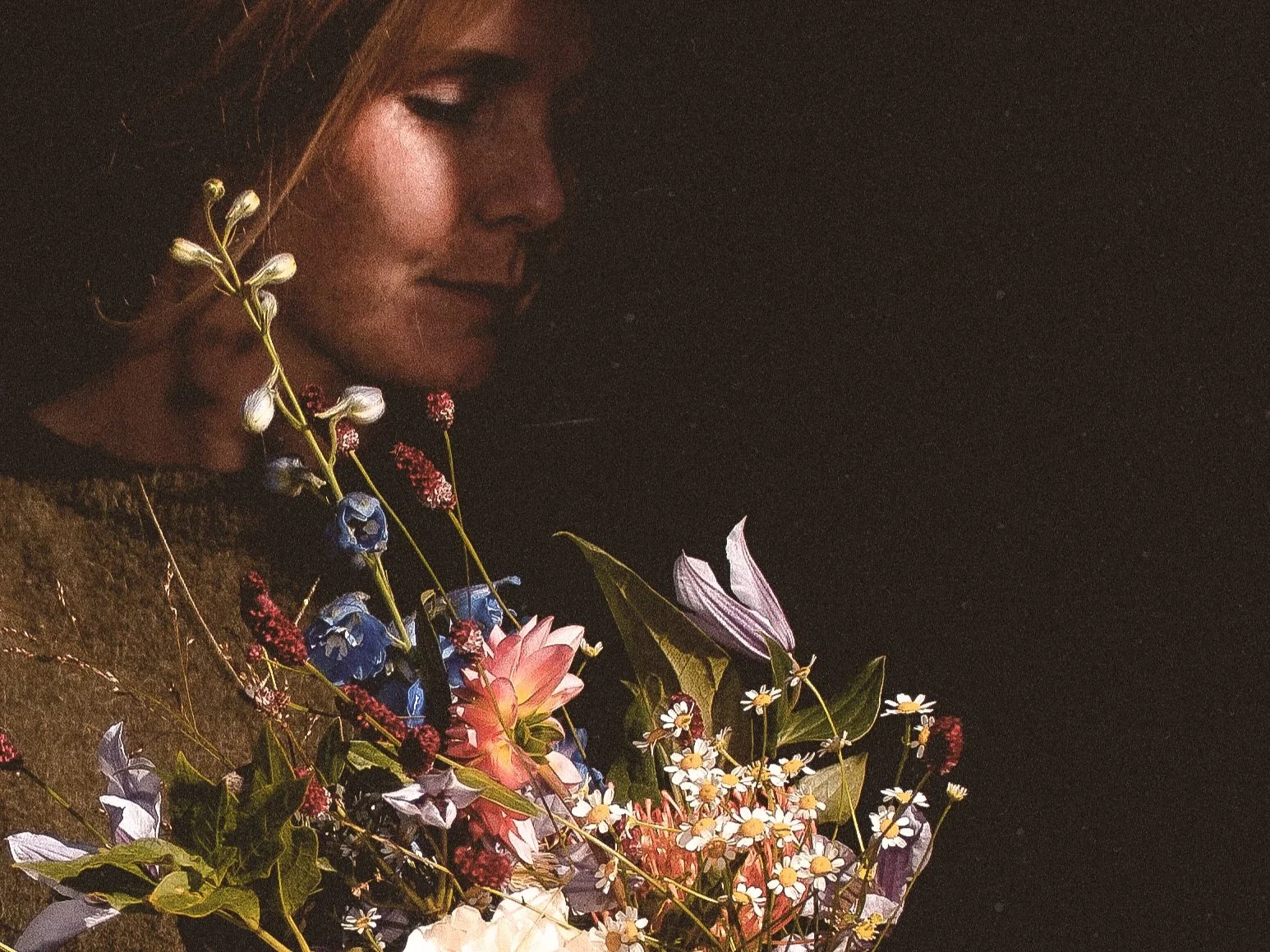 Close-up van een vrouw die op een zwarte achtergrond naar een boeket bloemen kijkt.