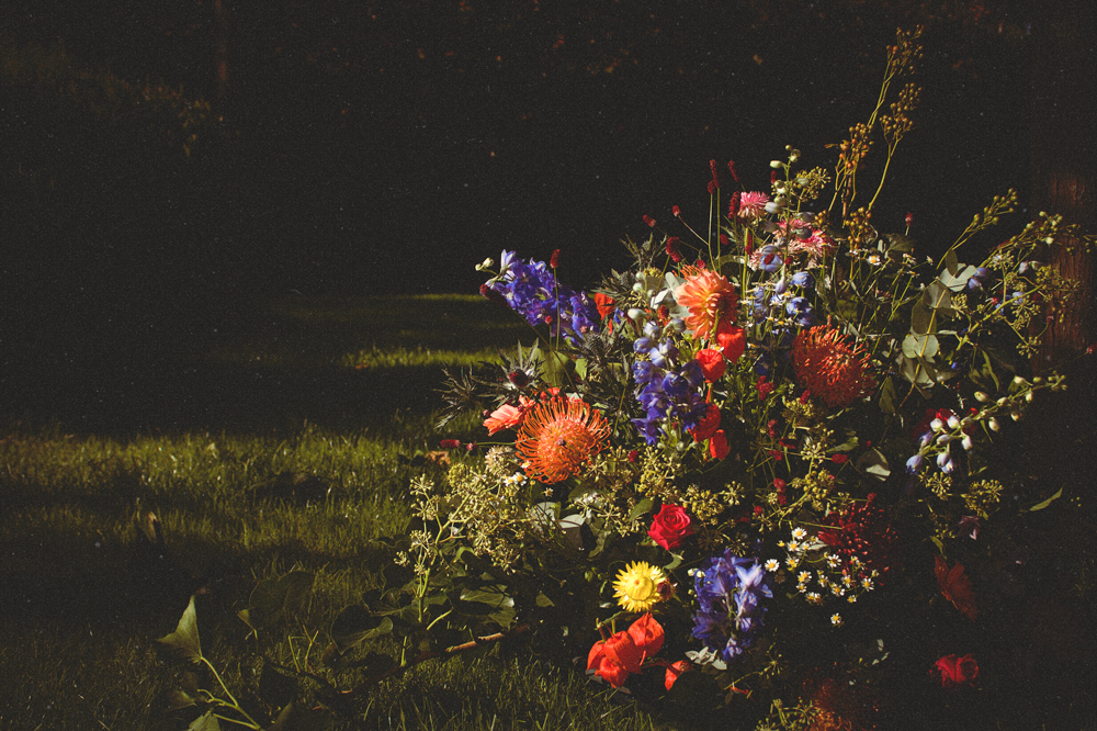 Laten bloemstuk met diverse kleurrijke bloemen, gelegen op gras, in een donkerdere achtergrond.