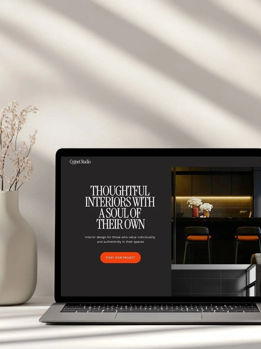 Contemporary interior design website homepage displayed on a modern laptop, showing the hero section with the call to action 'Start Your Project'. The visual features a dark, luxurious kitchen interior with orange and white accents.