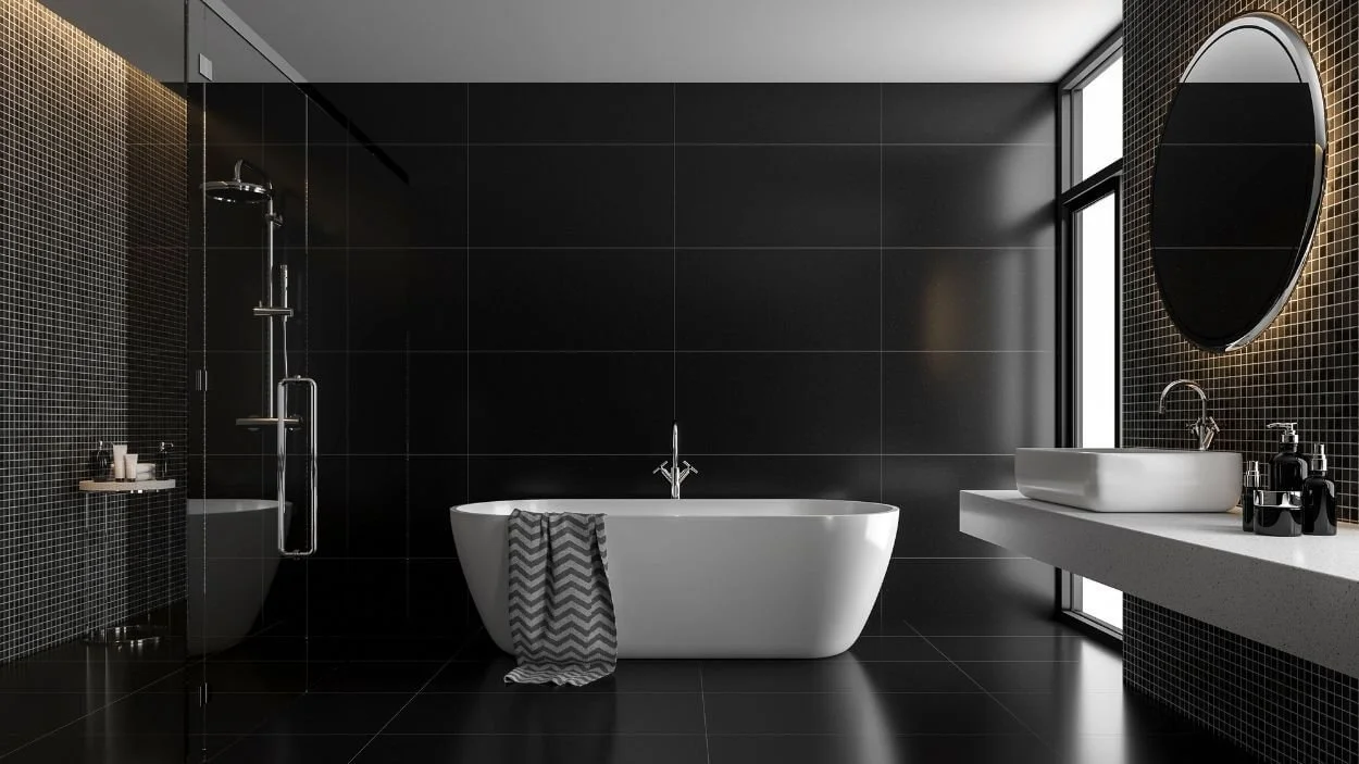 A luxurious modern bathroom dominated by black tiling. It features a sleek white freestanding bathtub, a glass shower enclosure, a white floating sink, and a large circular mirror with subtle backlighting.
