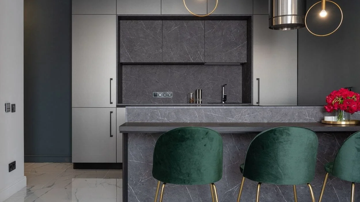 Photo of a luxurious, modern kitchen with dark marble counters and island, and deep green velvet bar stools for "Green & Pine" a custom builder/architecture website template.