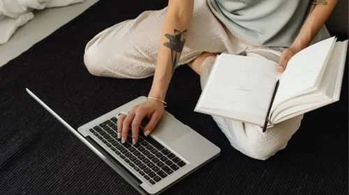 Woman sitting on the floor with a notepad, pen and laptop intentionally planning her website redesign.