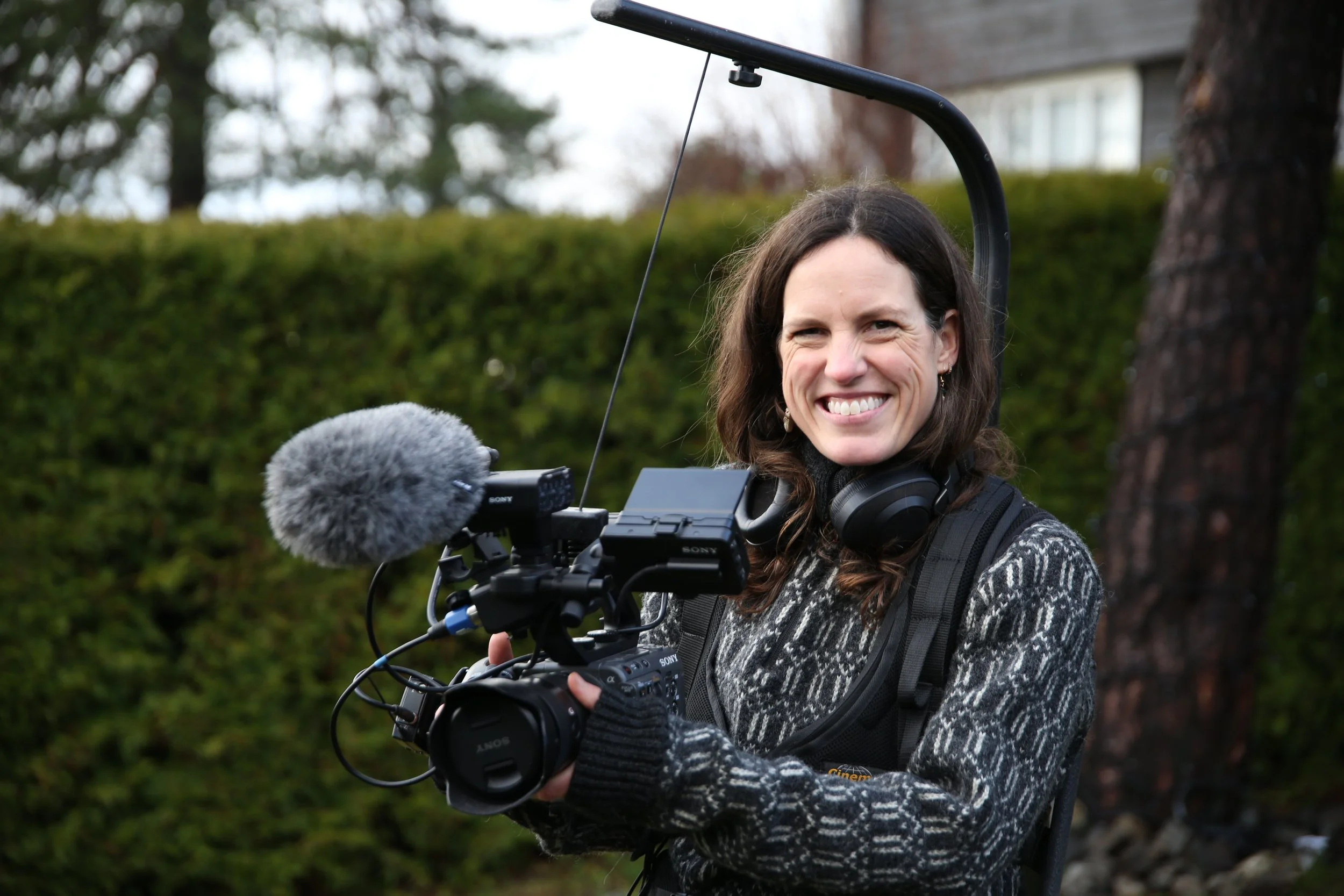 Stills bilde fra filmen "Mysteriepakken". Bilde av en kvinne som holder kamerautstyr og smiler mot kamera. 