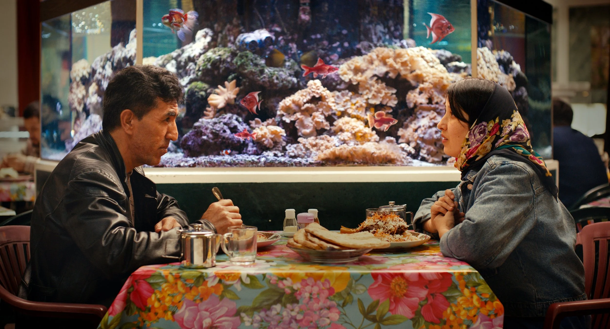 Bilde av en mann og en kvinne som sitter og spiser sammen på en restaurant. Det er mat på bordet og et stort akvarium i bakgrunnen. Mannen og kvinnen ser på hverandre.