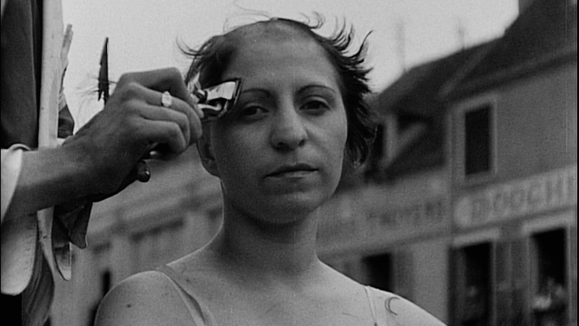 Still bilde fra filmen "De rettsløse". På bilde er det en kvinne fra andre verdenskrig. Kvinnen blir skamklipt og ser alvorlig ut på kamera. Bildet er i svart og hvitt. 