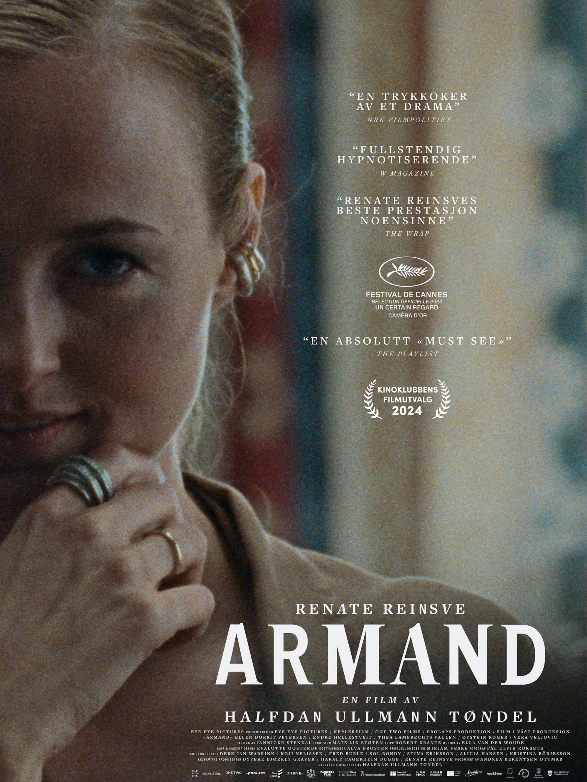 Filmplakat for filmen 'Armand' med et nært bilde av en kvinne som har blondt hår, gullringer, og en myk men fascinert uttrykk, med tekster og priser i bakgrunnen.