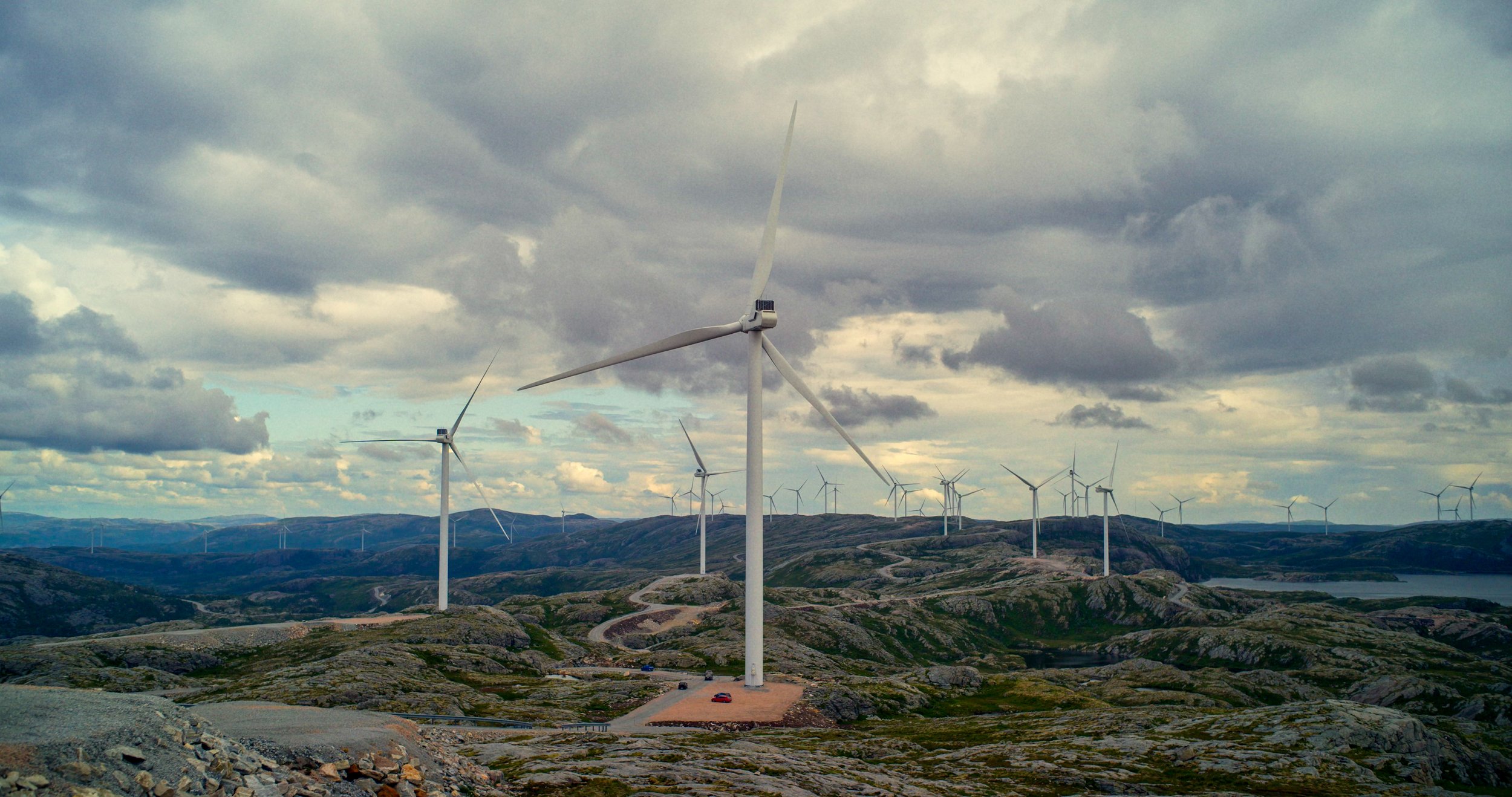 Et bilde av et fjell-landskap. På fjellet er det mange vindmøller spredt utover naturen. I himmelen er det mange skyer.