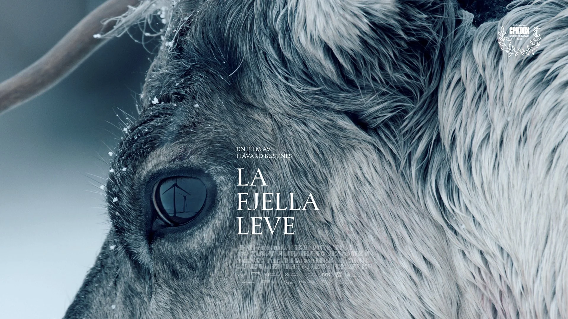 En filmplakat for filmen La Fjella Leve. Nærbilde av øyene til et reinsdyr. Det er mørke toner med blått. I refleksjonen på øyet til reinsdyret er det en vindmølle. 