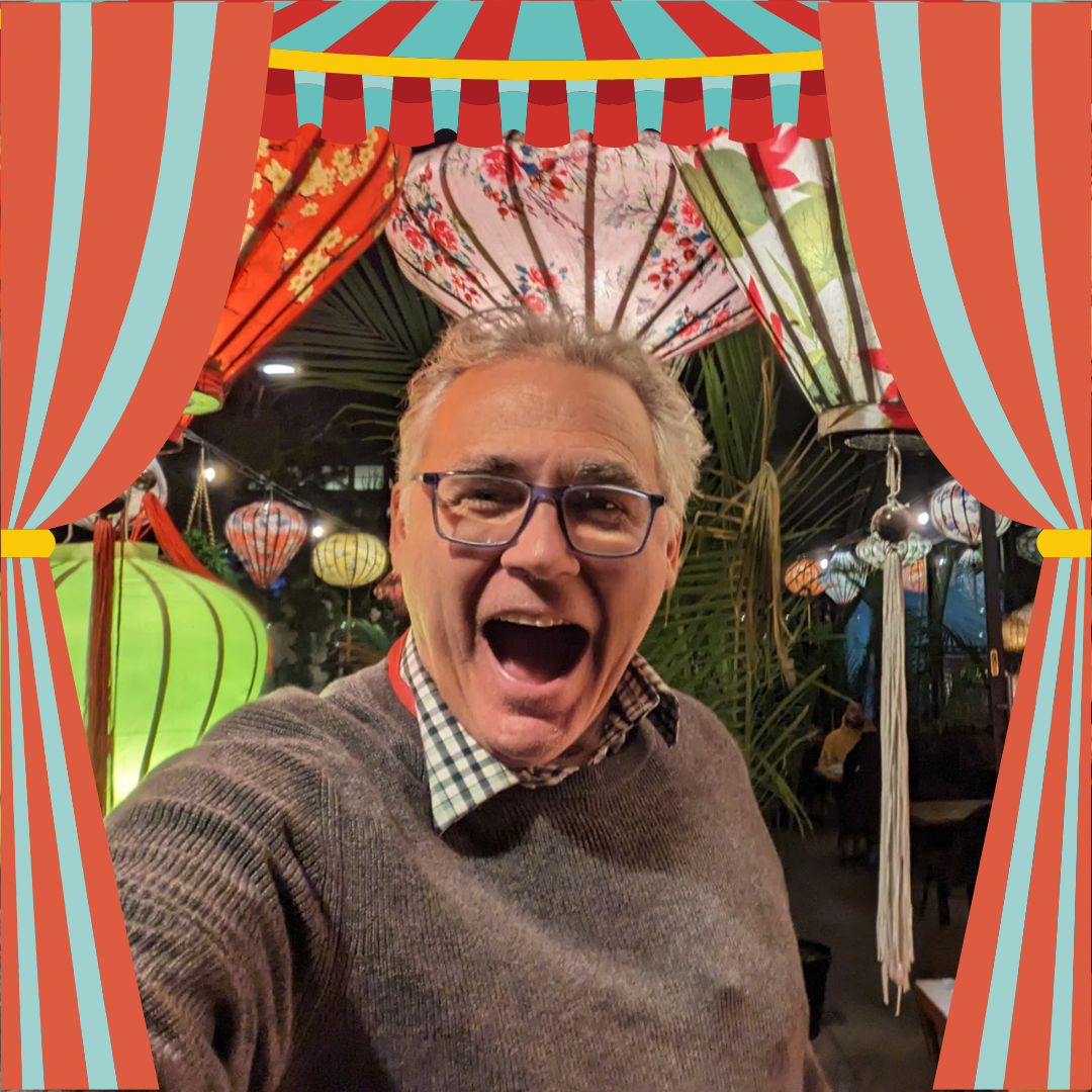 A man wearing glasses is laughing while looking into the camera.