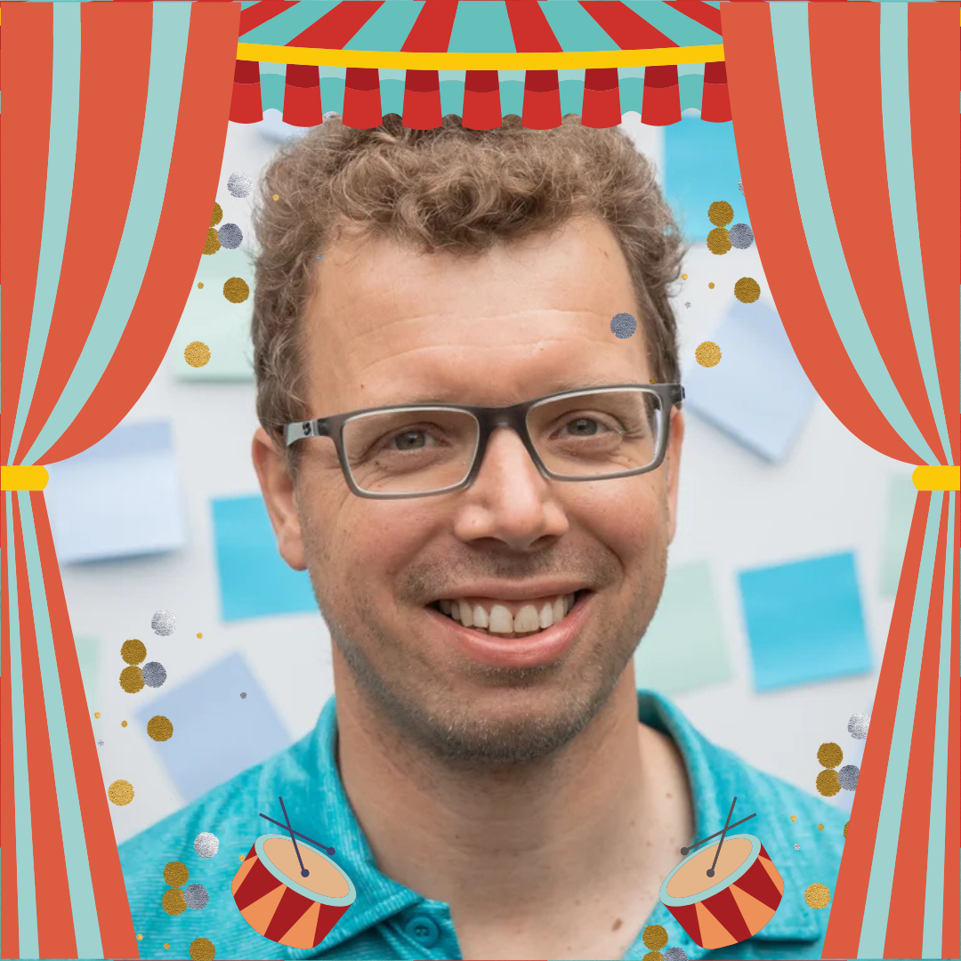 A man with glasses and curly hair smiling into the camera.