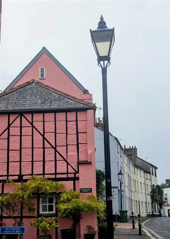 A pink building with a tall lamppost in the foreground, leading to a curved street with colourful buildings.
