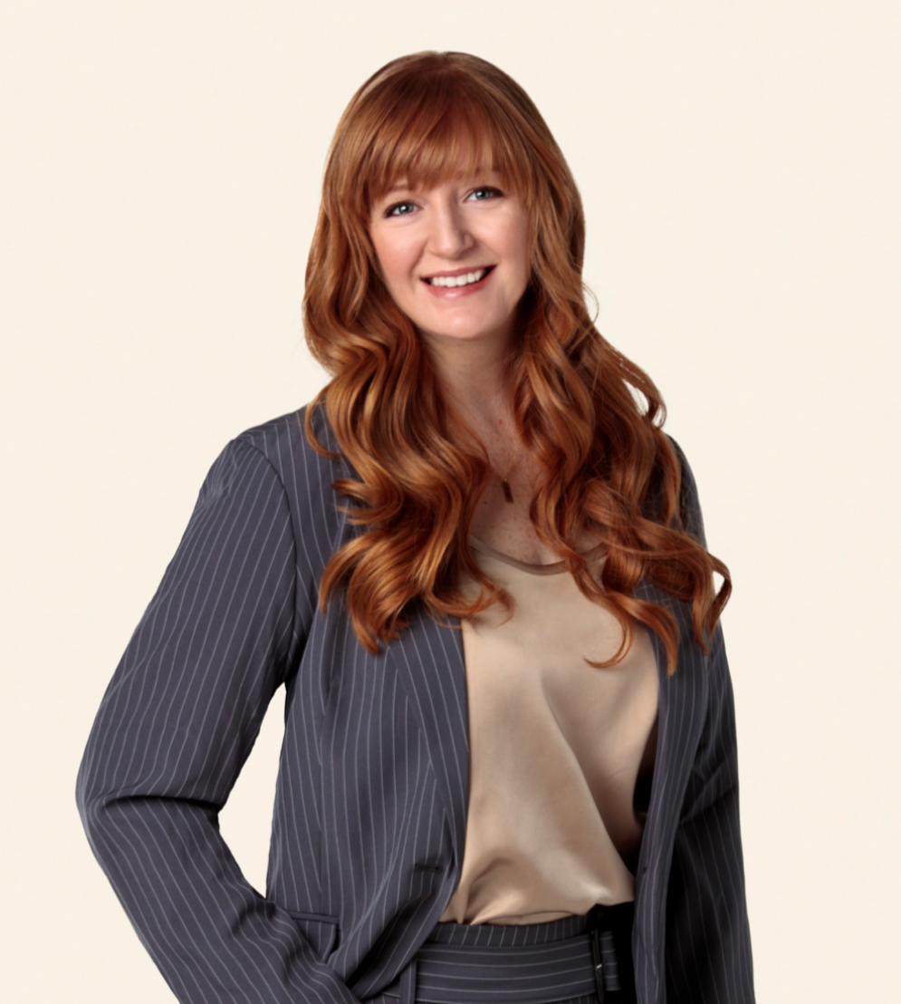 Christa in a blue suit with hand in pocket against a white wall