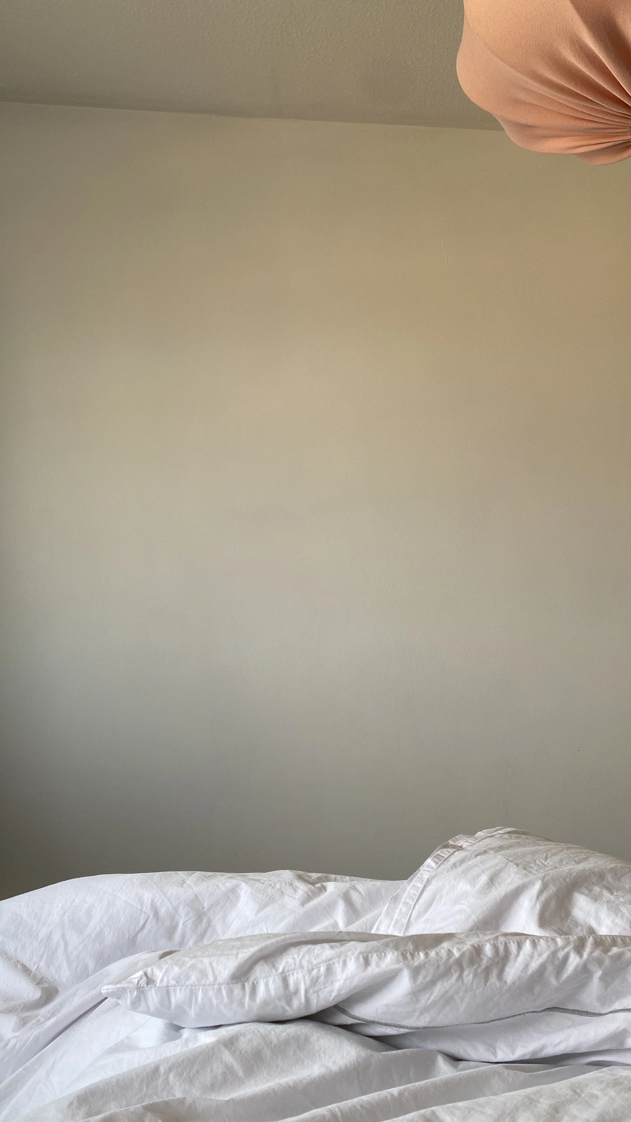 A photo of the view from bed, white sheets, white wall and pink lampshade