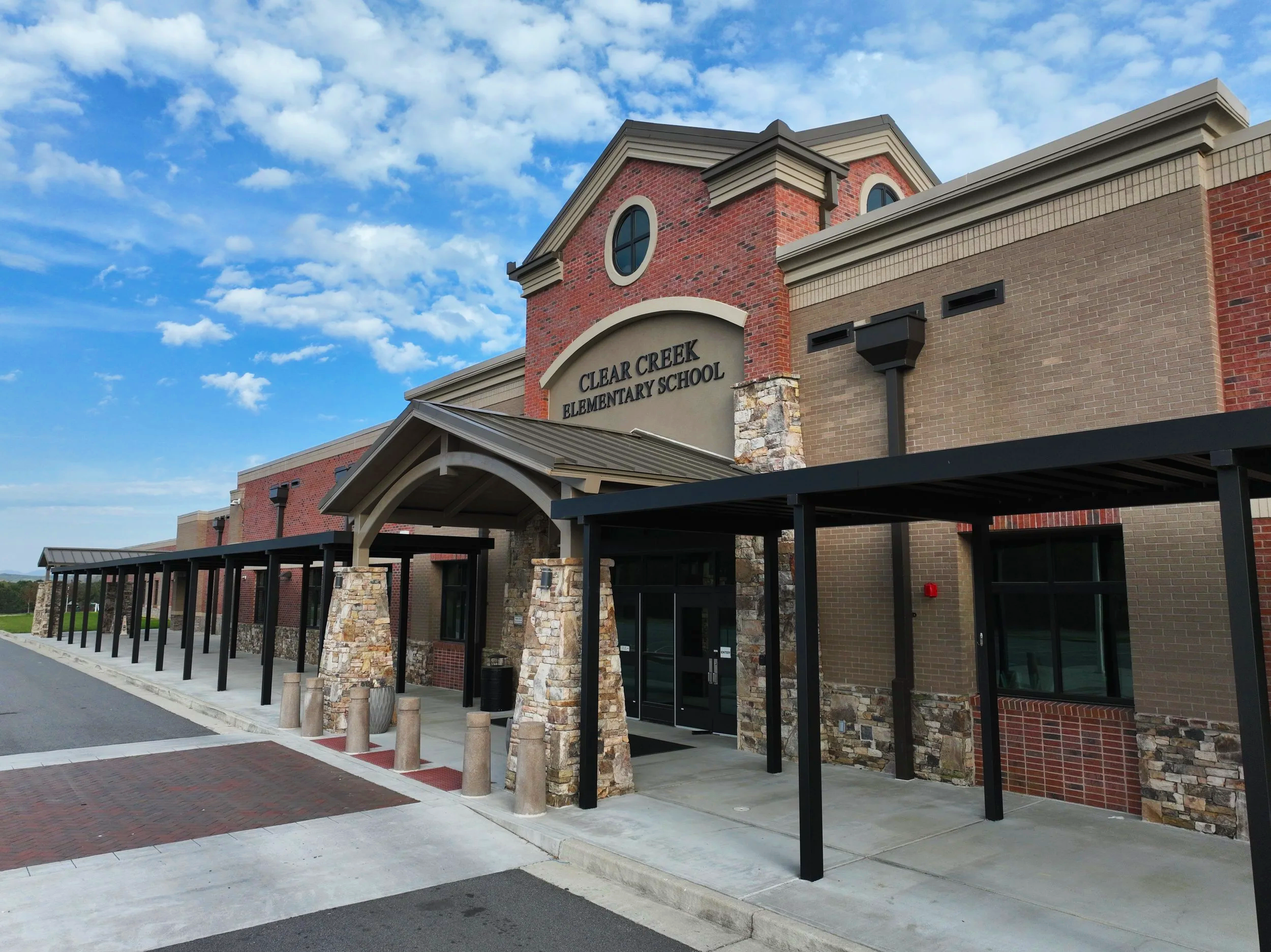 Front view of Clear Creek Elementary School building with brick and stone exterior, canopy entrance, and a blue sky with clouds.