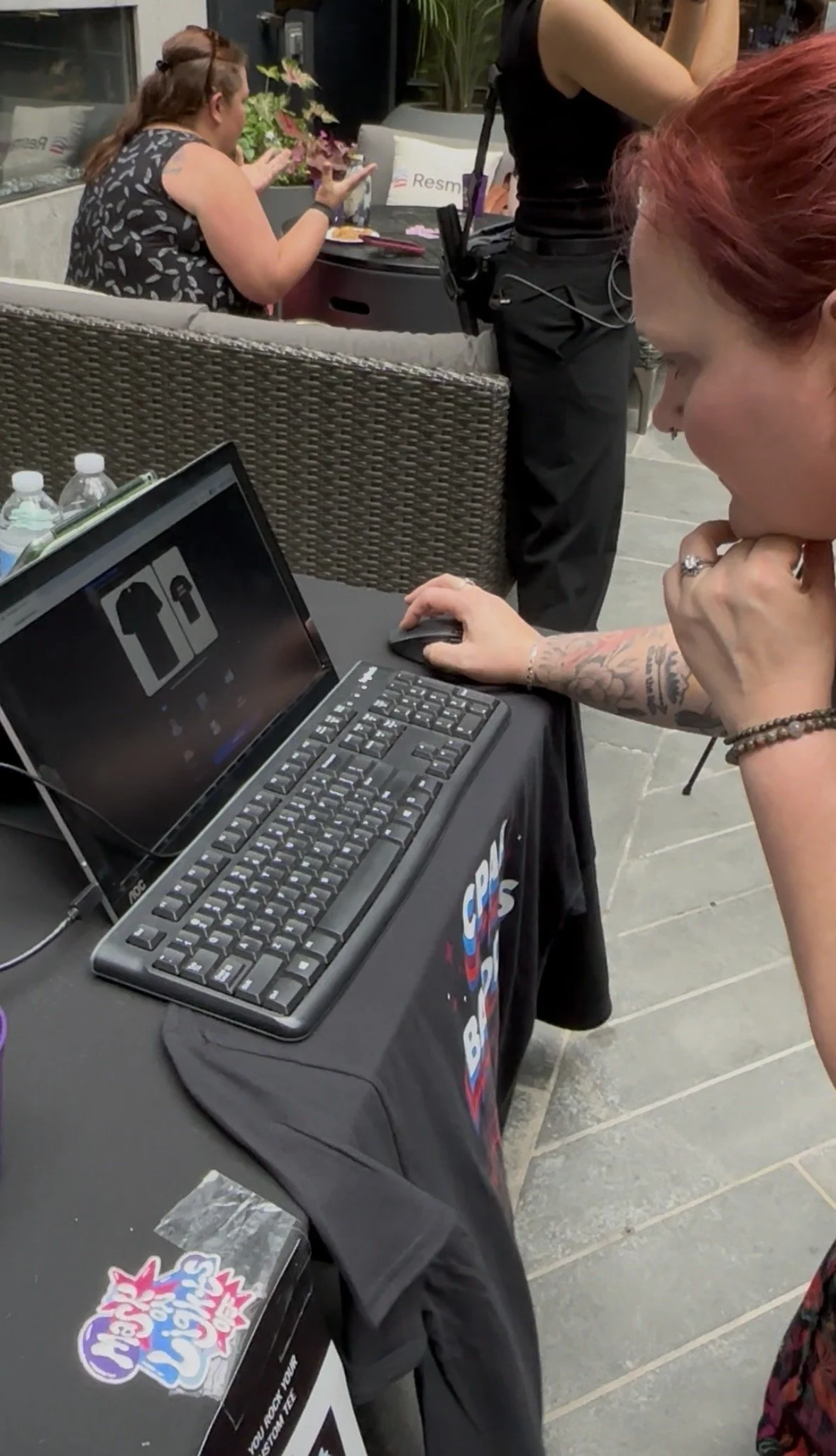 A man using a touchscreen to design a T-shirt at a crowded trade show or conference.
