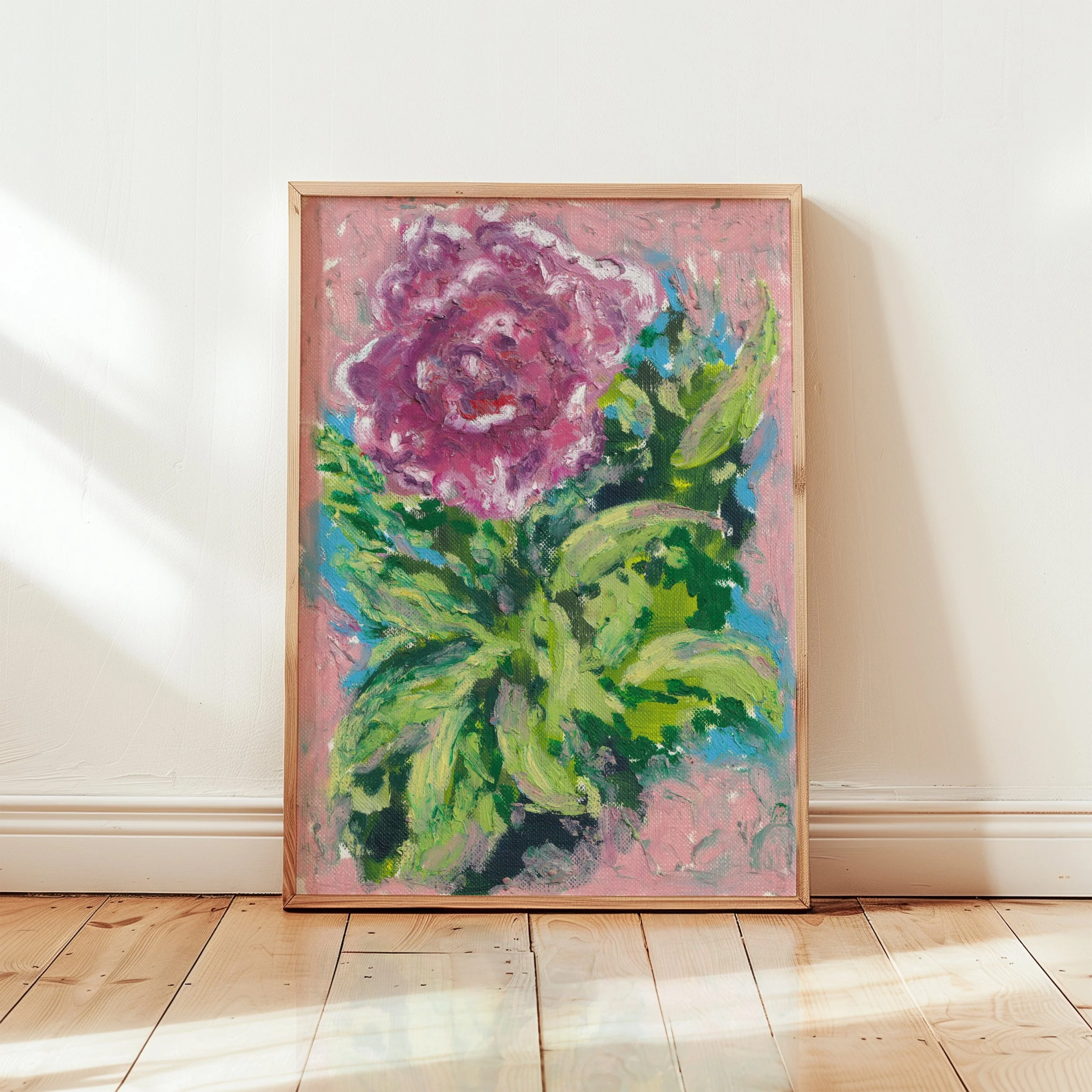 A framed abstract painting of a pink and purple flower with green leaves, leaning against a white wall on a wooden floor.