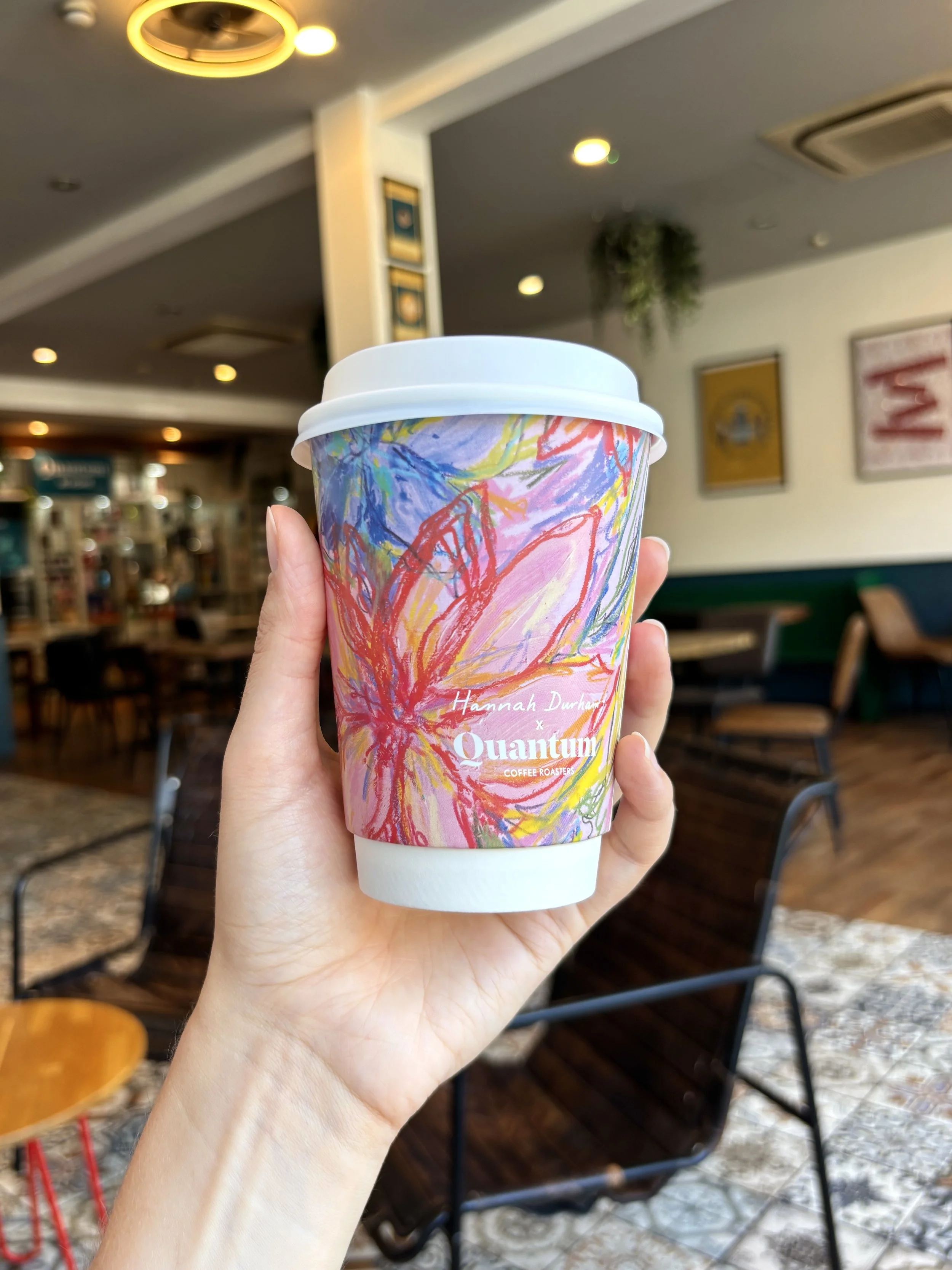 Ahand holding a colourful designed takeaway coffee cup