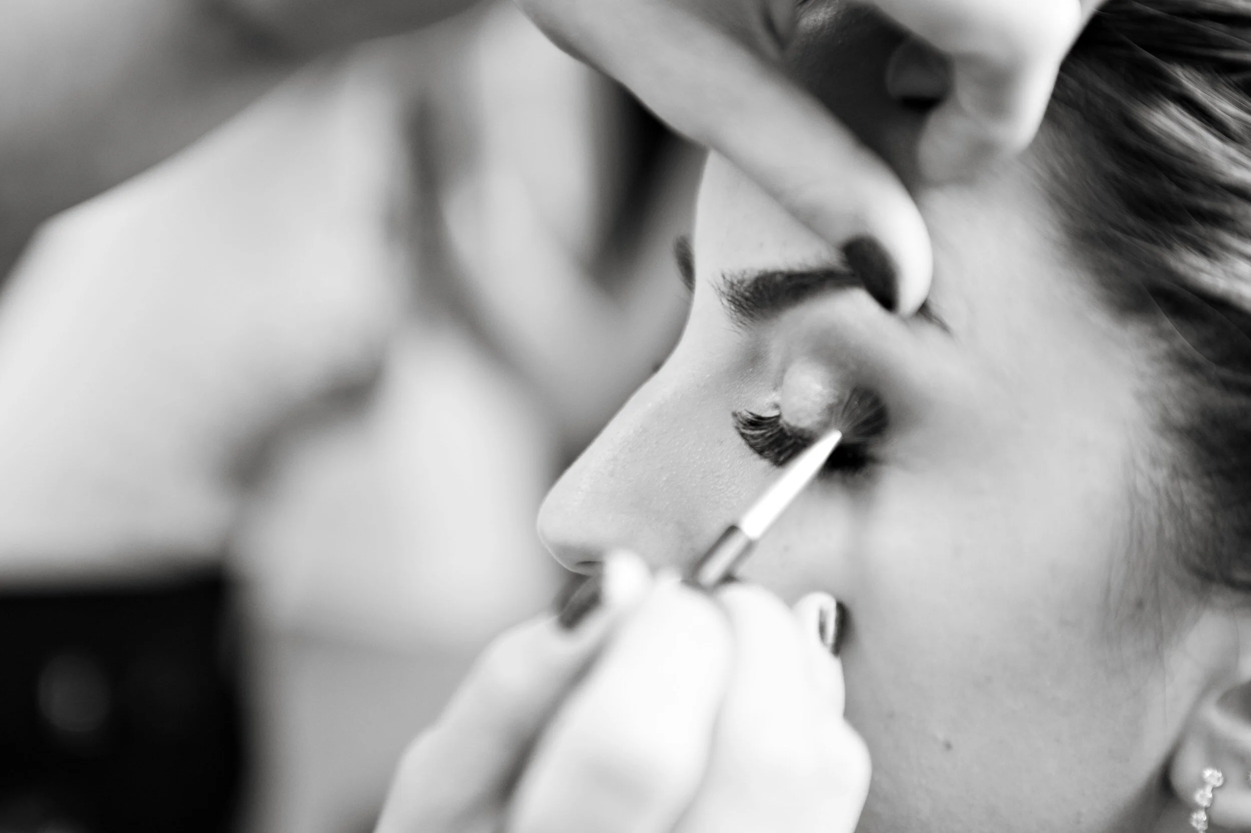 Close-up of a person applying eyeshadow with a brush on a woman's eyelid.