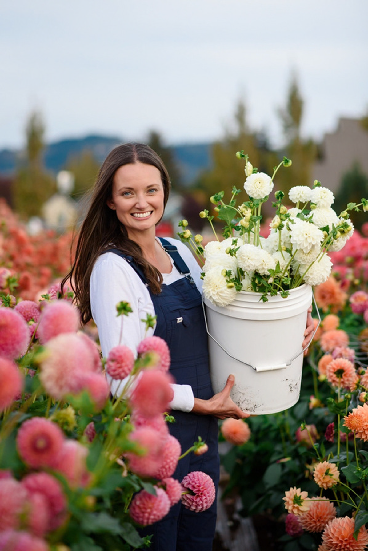 Woman holding a bucket of white flowers in a colorful flower garden