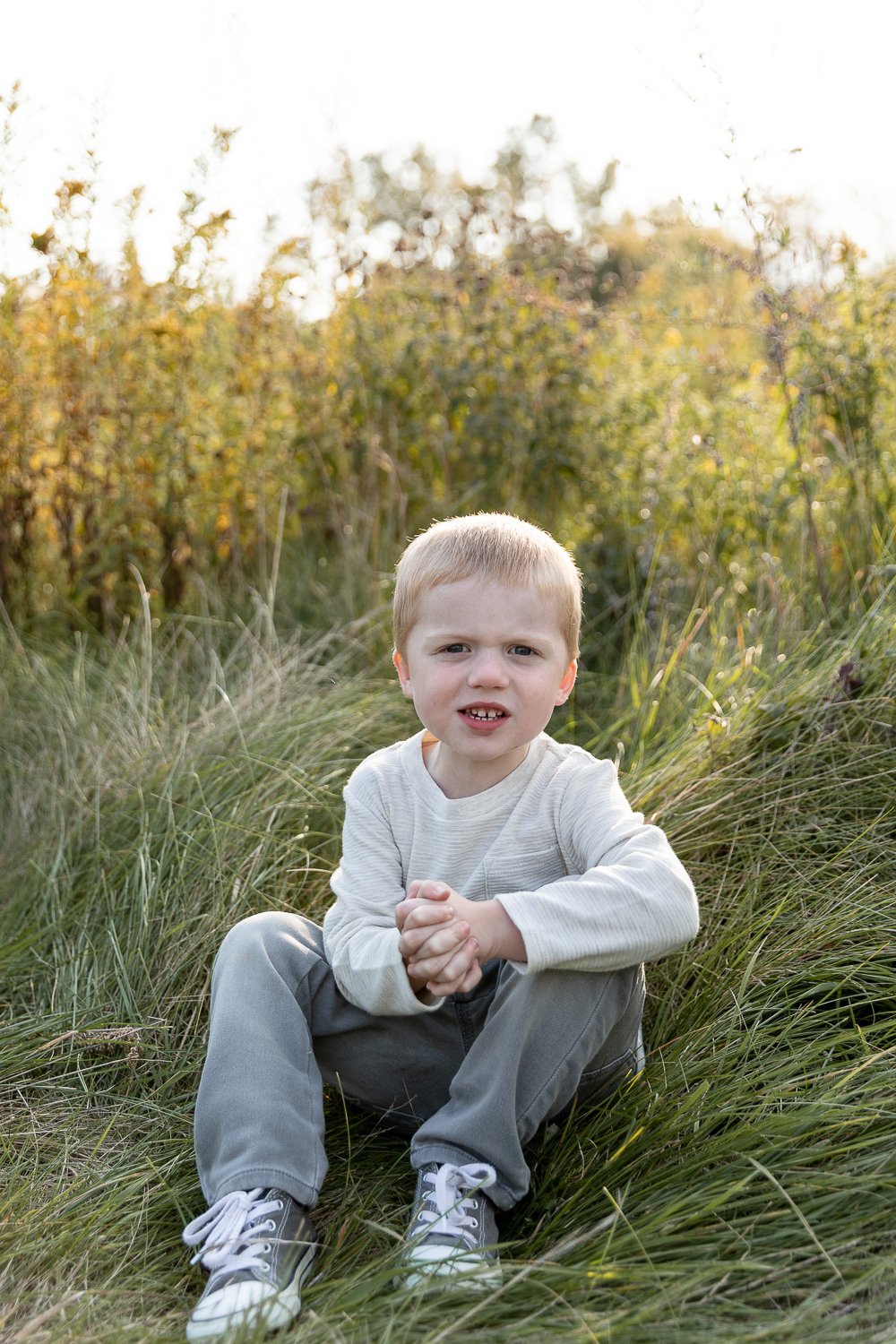 individual photo of young boy sitting on the grass wit his hands together during brookfield family photo session with grace creatives photography