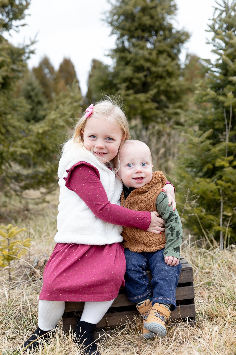 young brother and sister sitting on a crate during tree farm mini session with grace creatives