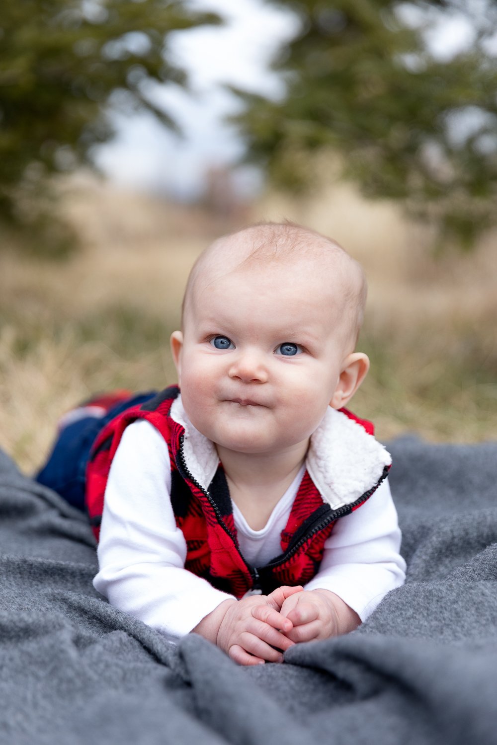 6 month baby laying down on a blanket while wearing a red and black plaid vest