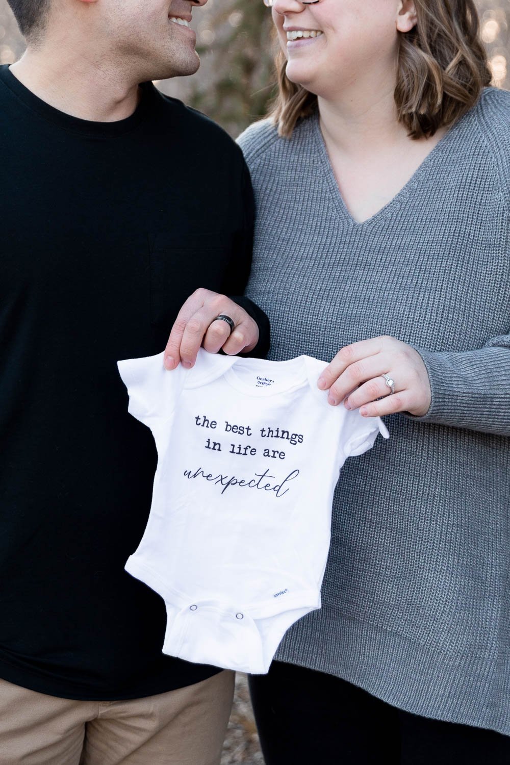 Mother and father with onesie that says "the best things in life are unexpected"