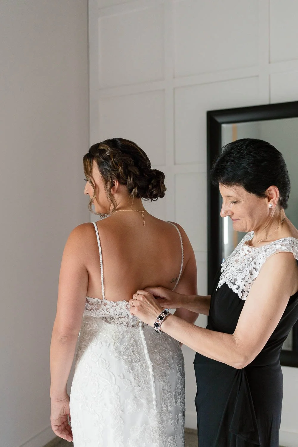 Mom buttoning up bride's dress