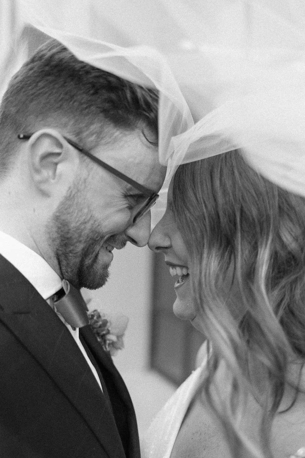 Black and white image of bride and groom forehead to forehead under veil