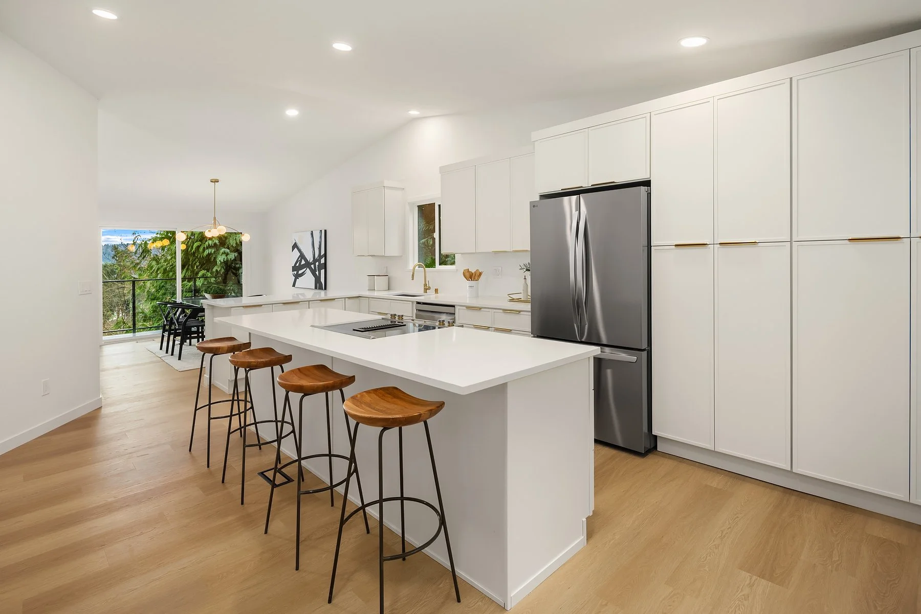 A modern kitchen renovation project with white island, black hardware, pendant lights, and hardwood floors, open to dining and living areas with large windows and ceiling lights.