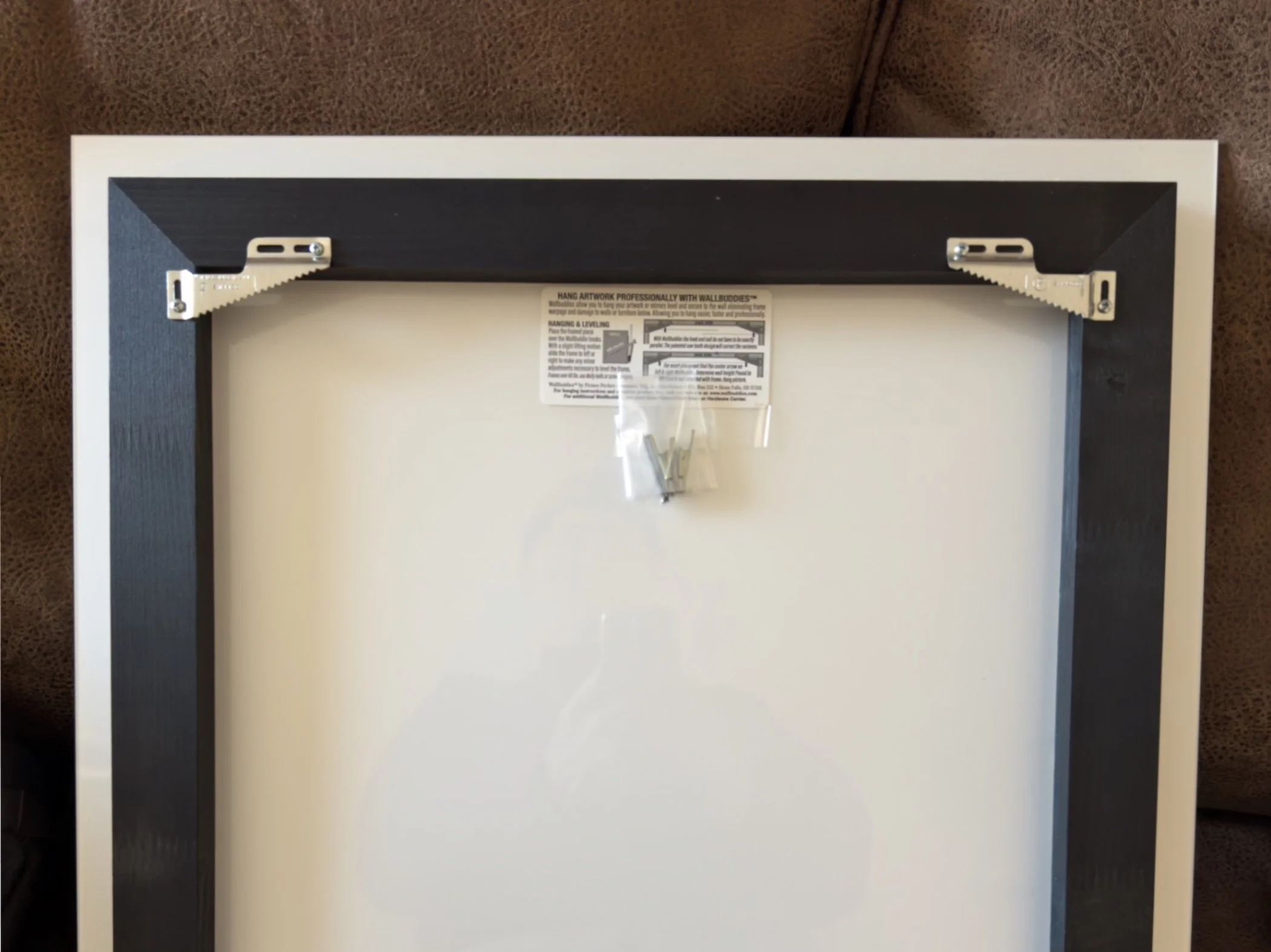 Back of a picture frame with hanging hardware and mounting hardware attached, viewed from above.