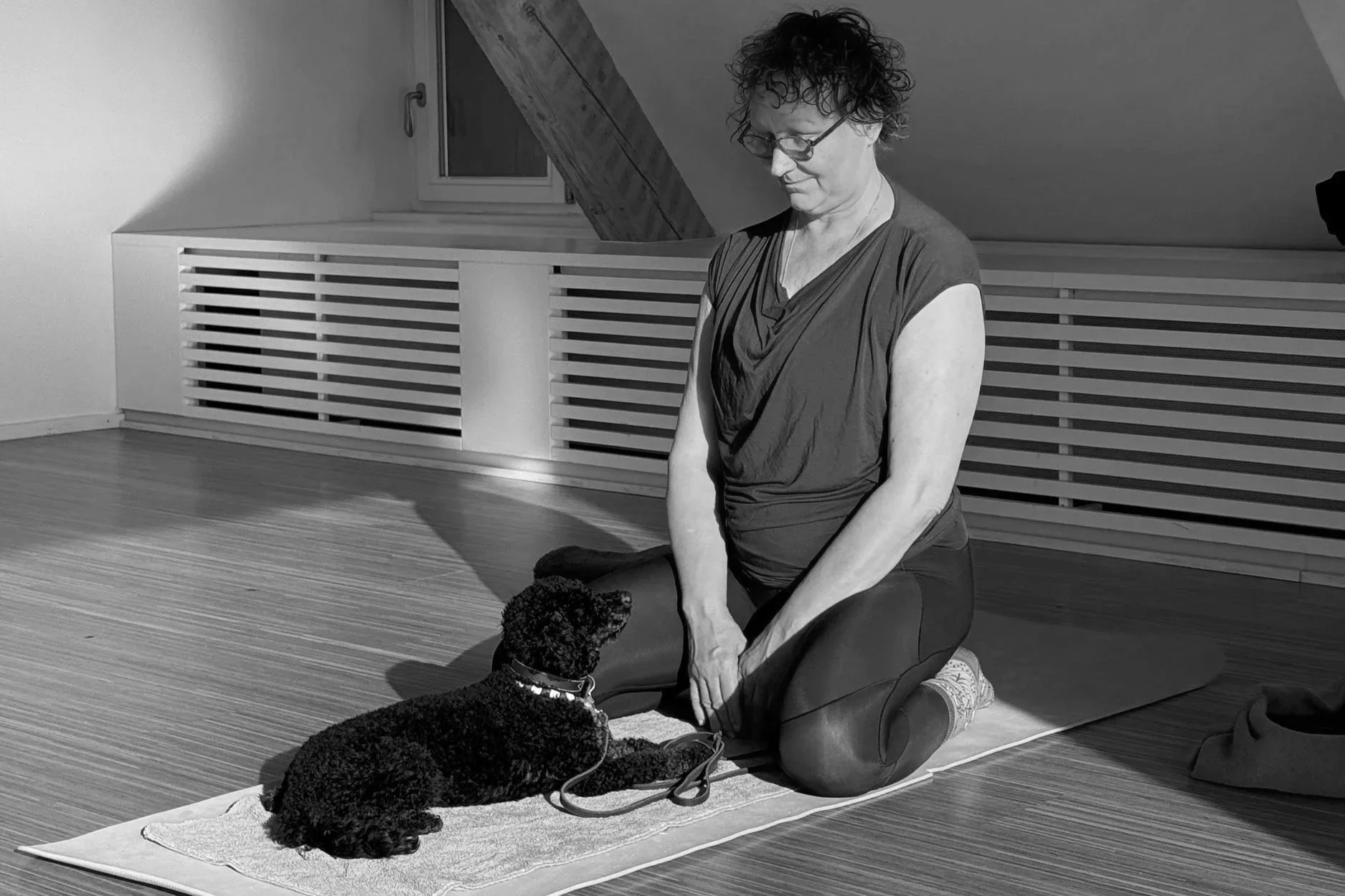 A person sitting on a mat indoors with a black dog lying in front of them.