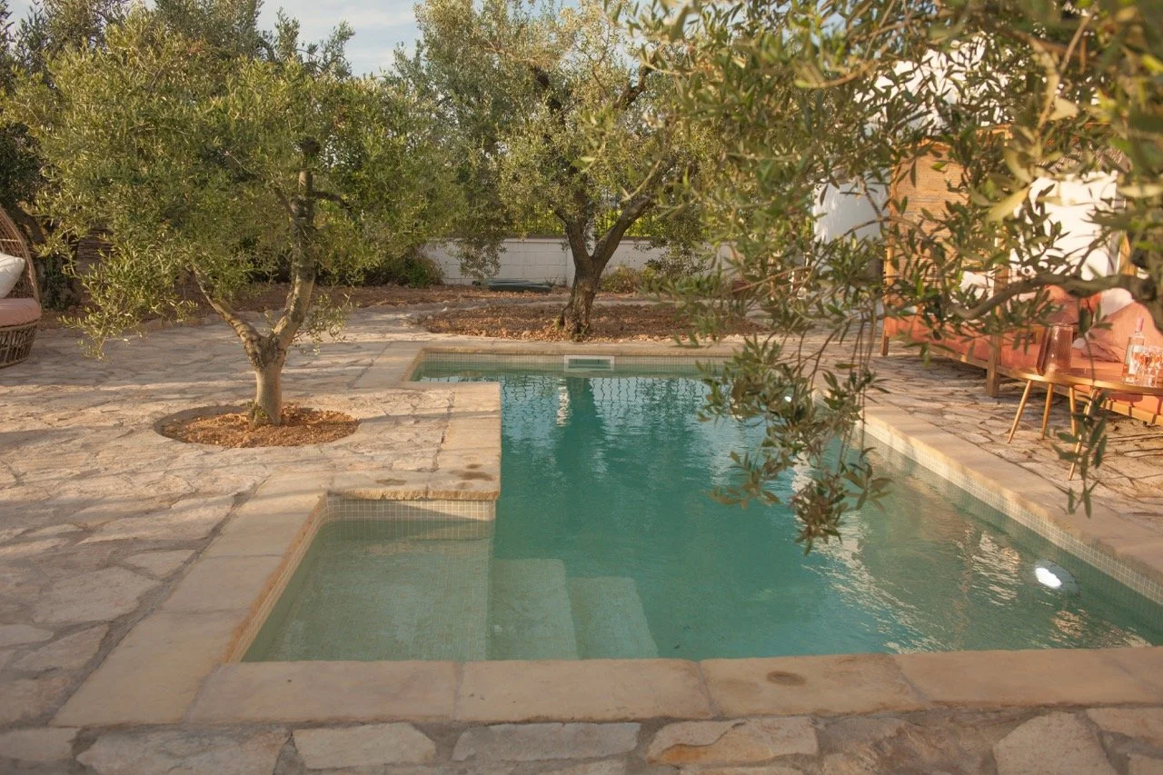 Ein kleiner Pool im Garten, umgeben von Steinen und Bäumen, mit Sitzgelegenheiten im Hintergrund.