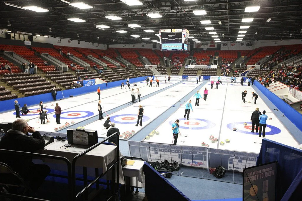 Interior of a curling rink during a competition with players on multiple lanes and spectators in the stands.