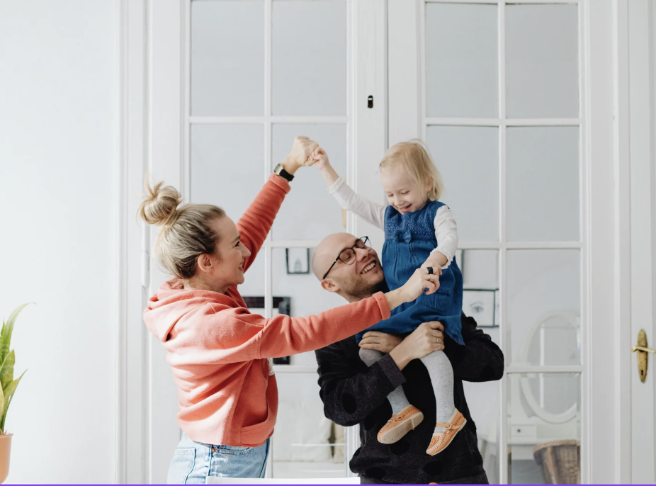A teacher and a man sitting with a young boy at a classroom table, reading a book together, with another woman and girl also present.