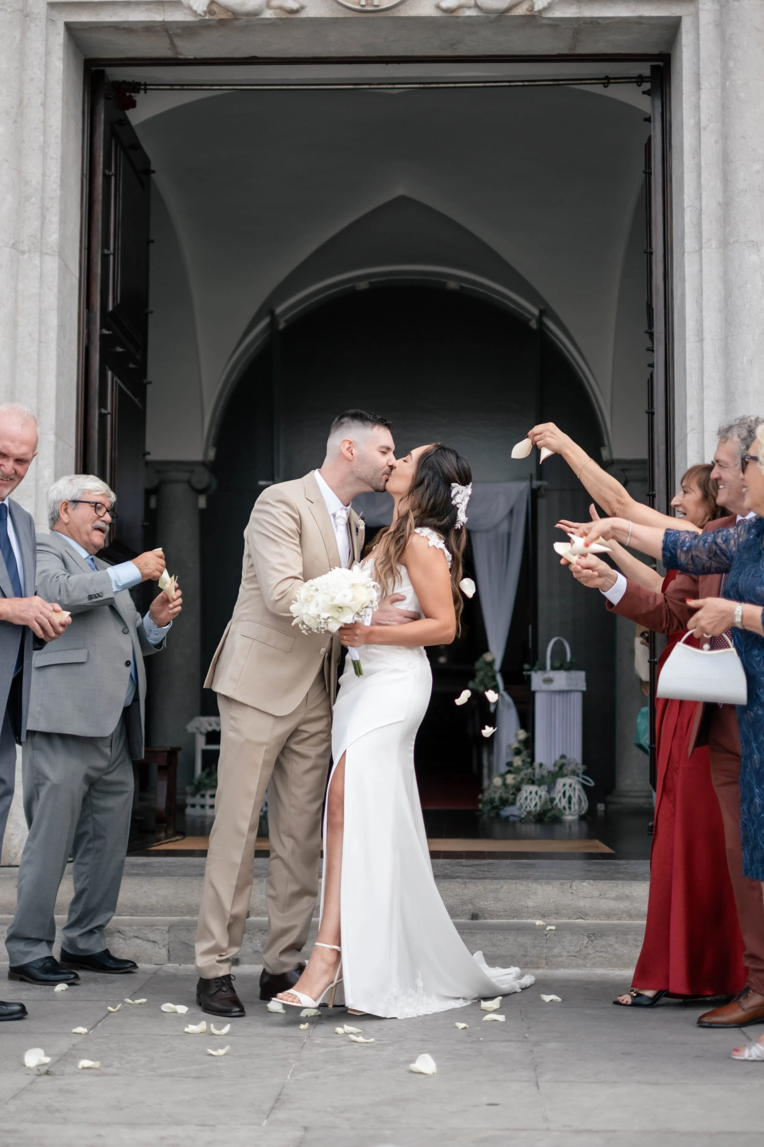 Noivos à saída da igreja rodeados por convidados e pétalas