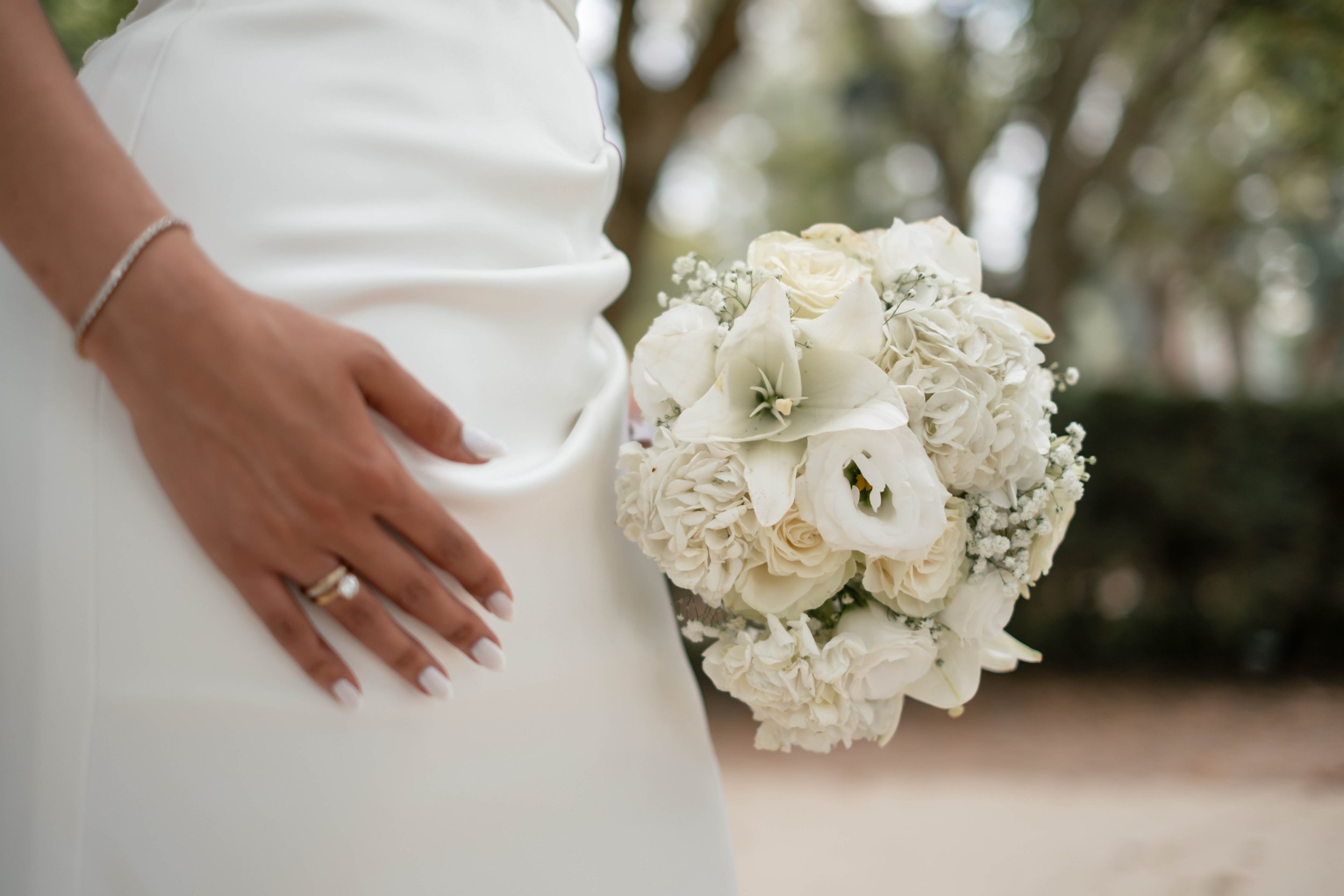 Detalhe da mão da noiva com aliança junto ao bouquet branco