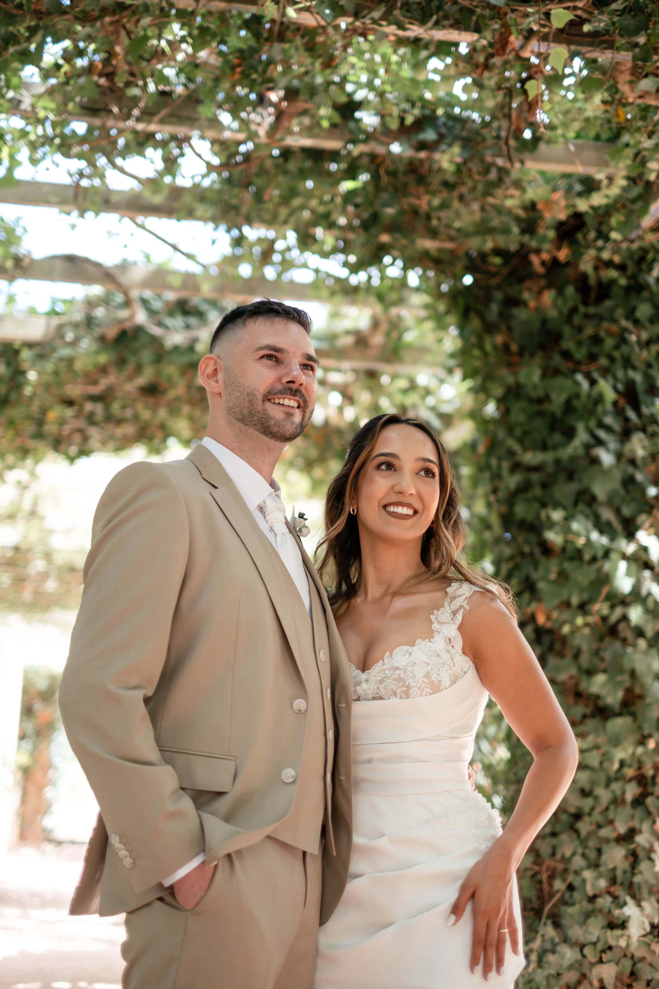 Noivos em retrato de casal sob uma pérgola com vegetação