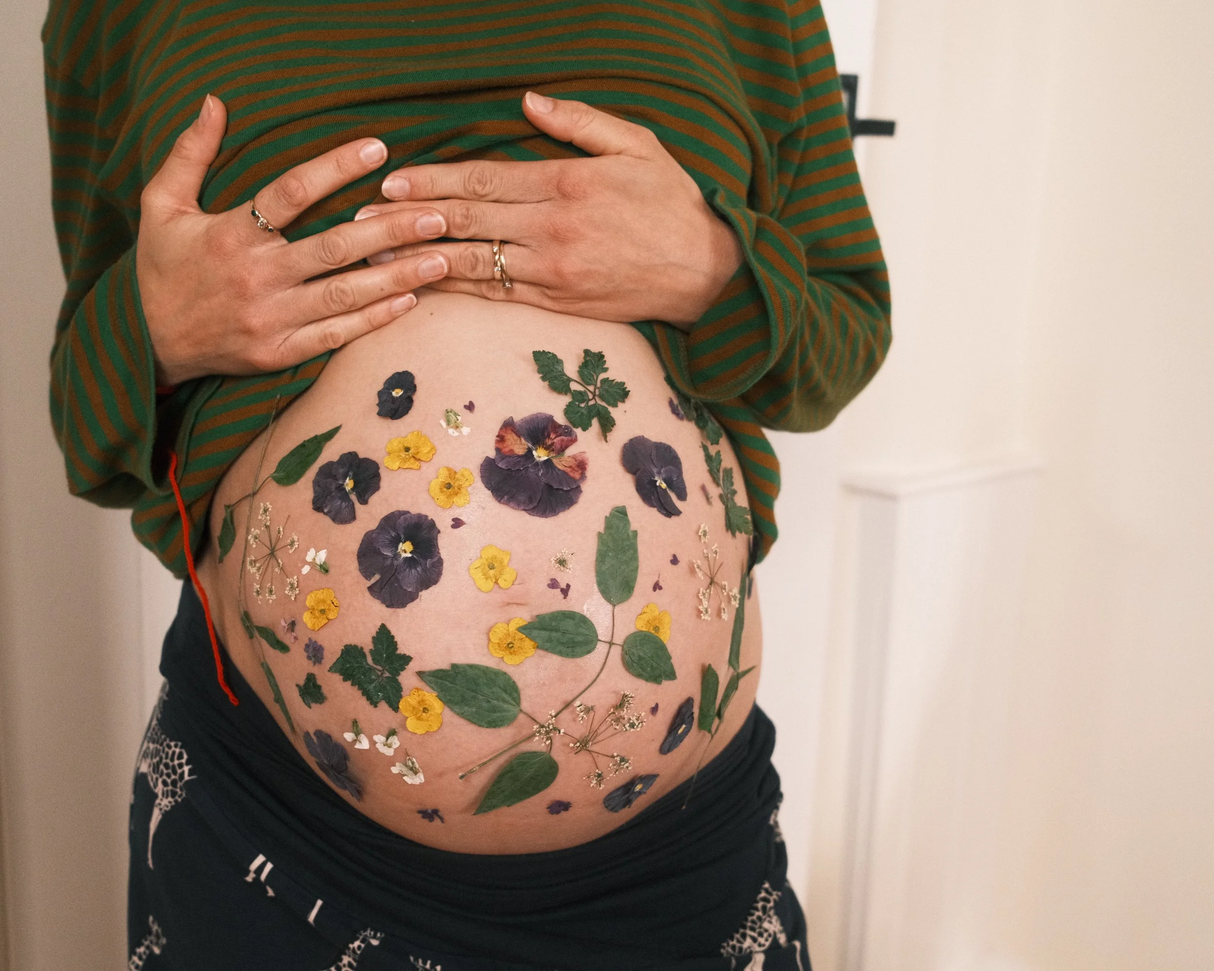 Woman lifting top to reveal baby bump decorated with pressed flowers