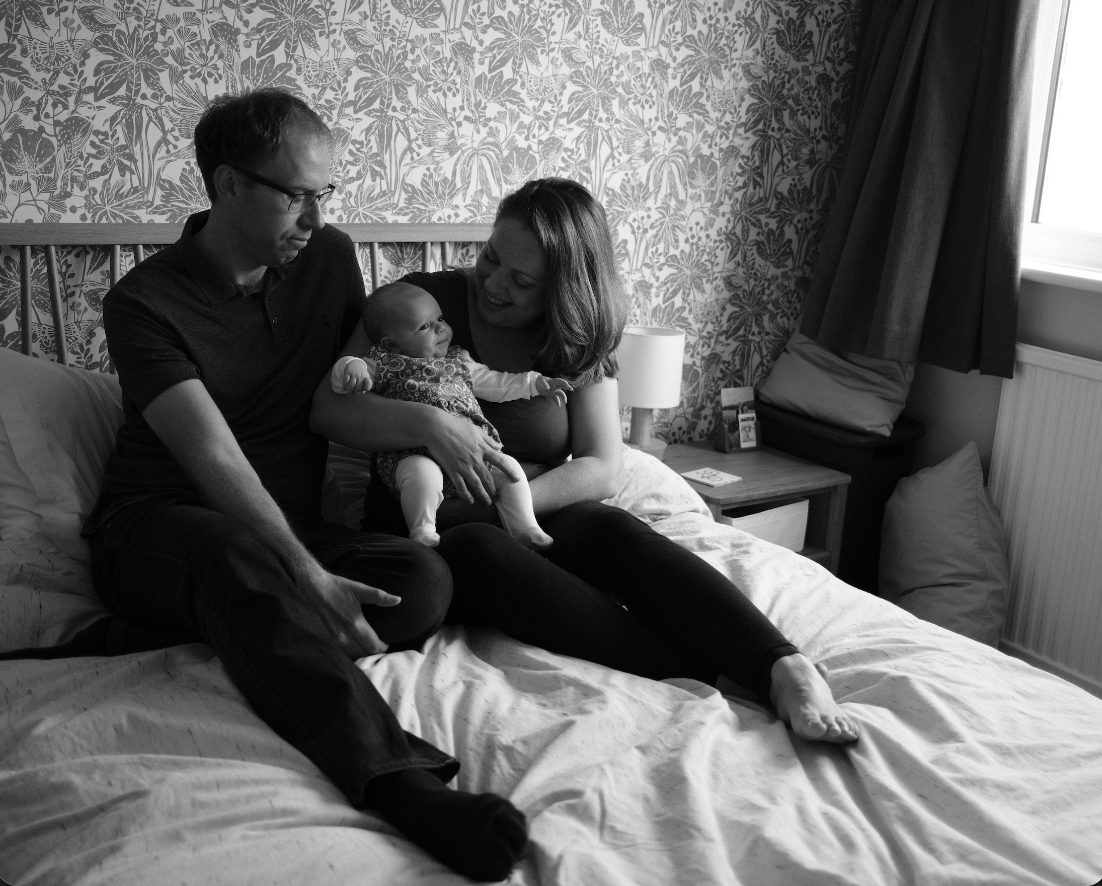 black and white image of mother and father sitting on a bed