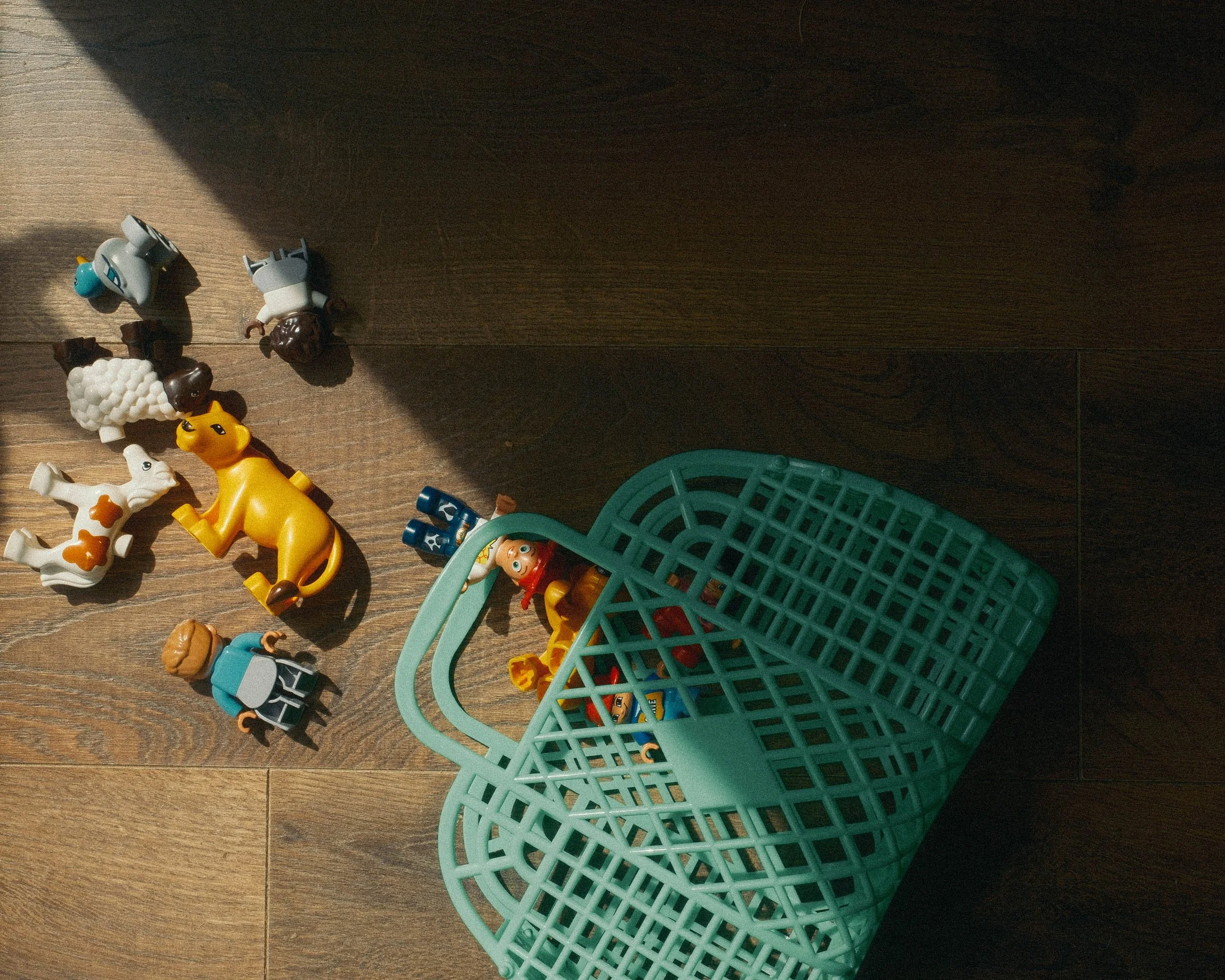 duplo toys spill out of a turquoise basket onto a wooden floor into a shaft of light